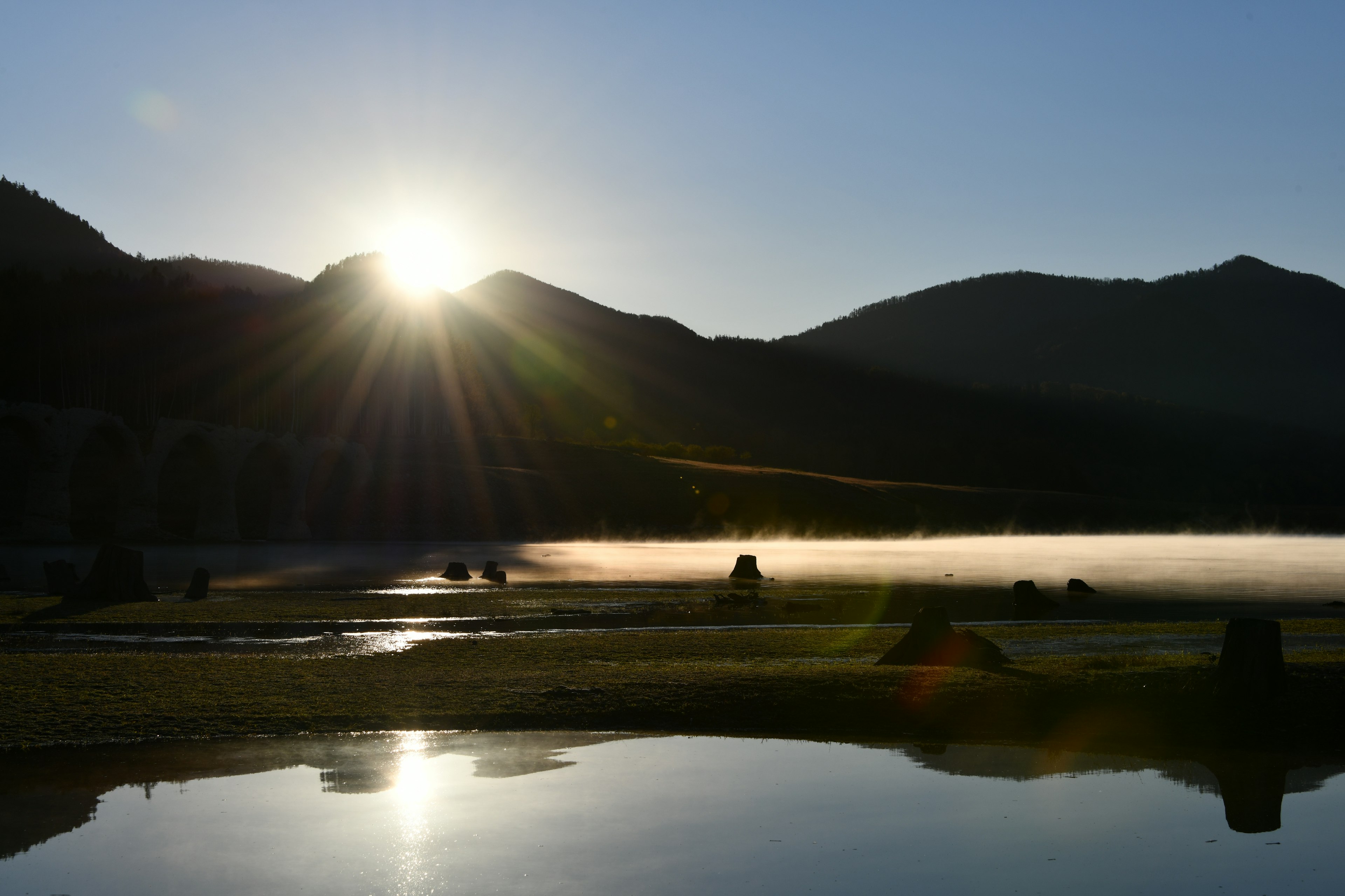 山々の間から昇る朝日と霧のかかった湖の風景