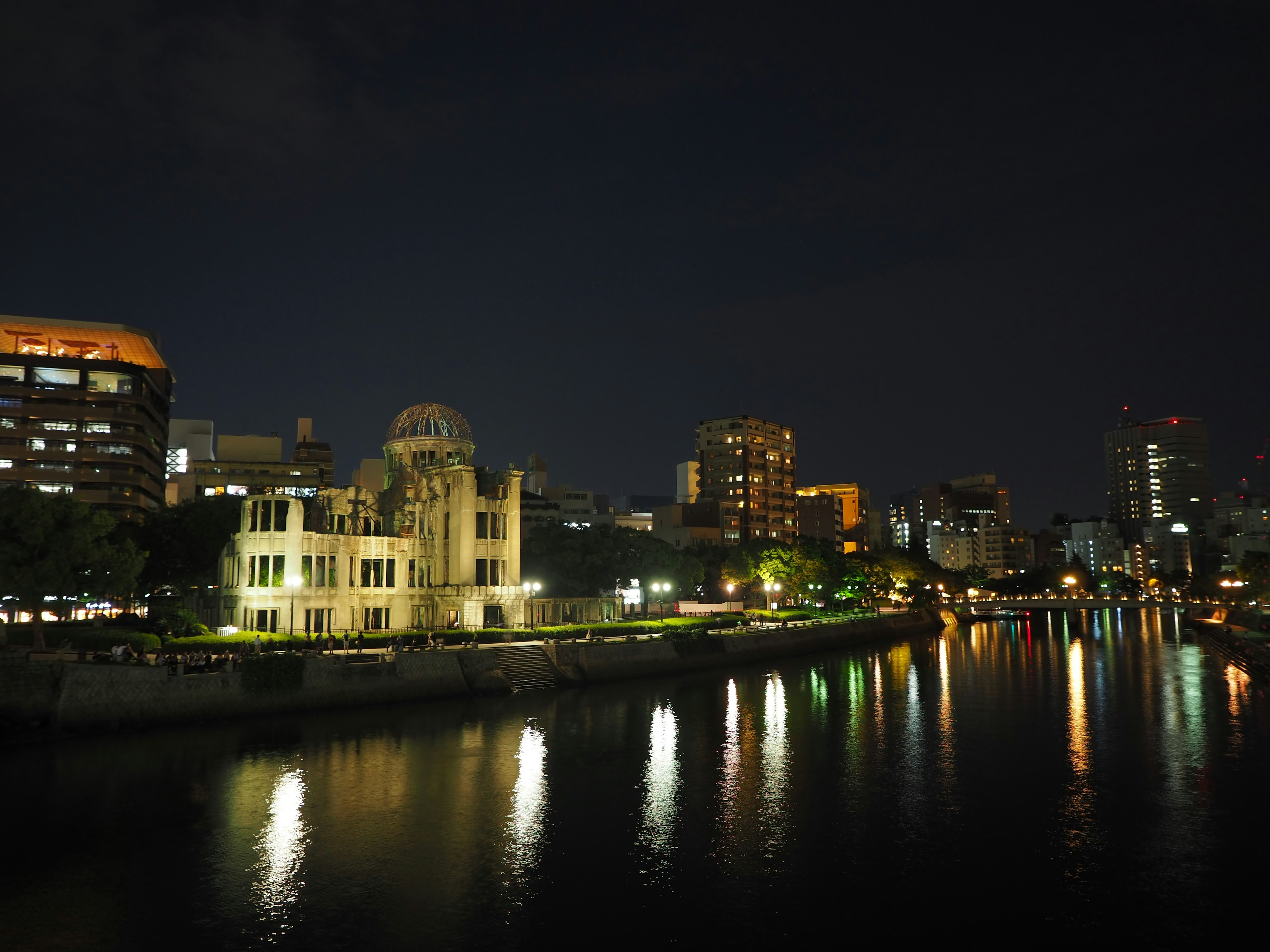 Atombombendome von Hiroshima entlang des Flusses bei Nacht mit modernen Gebäuden im Hintergrund