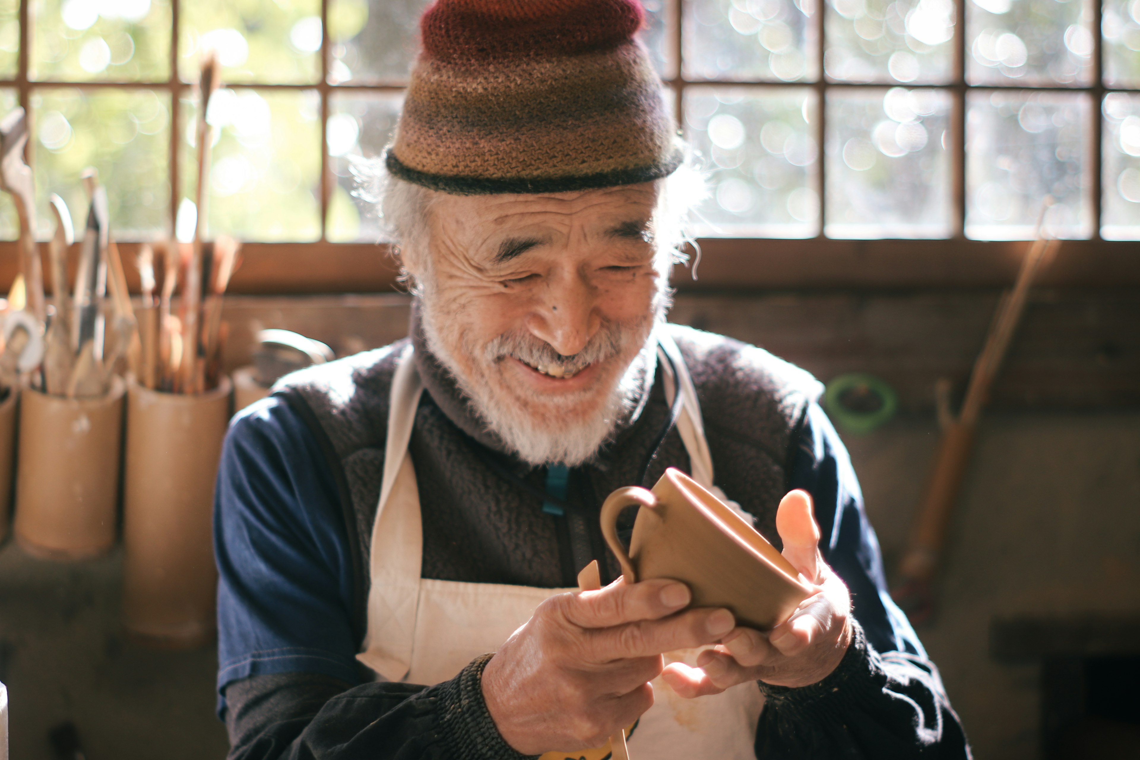 Artisan âgé souriant tenant une tasse en poterie dans un atelier