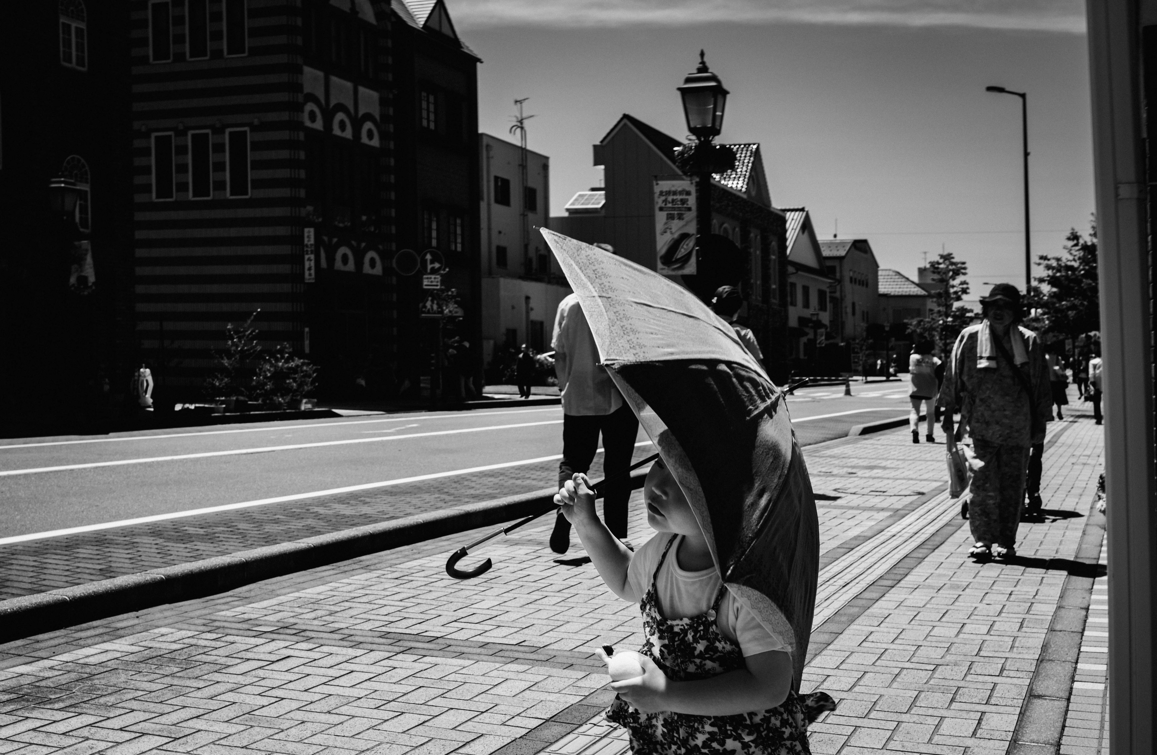 Una scena di persone che camminano per strada con una donna che tiene un ombrello in bianco e nero