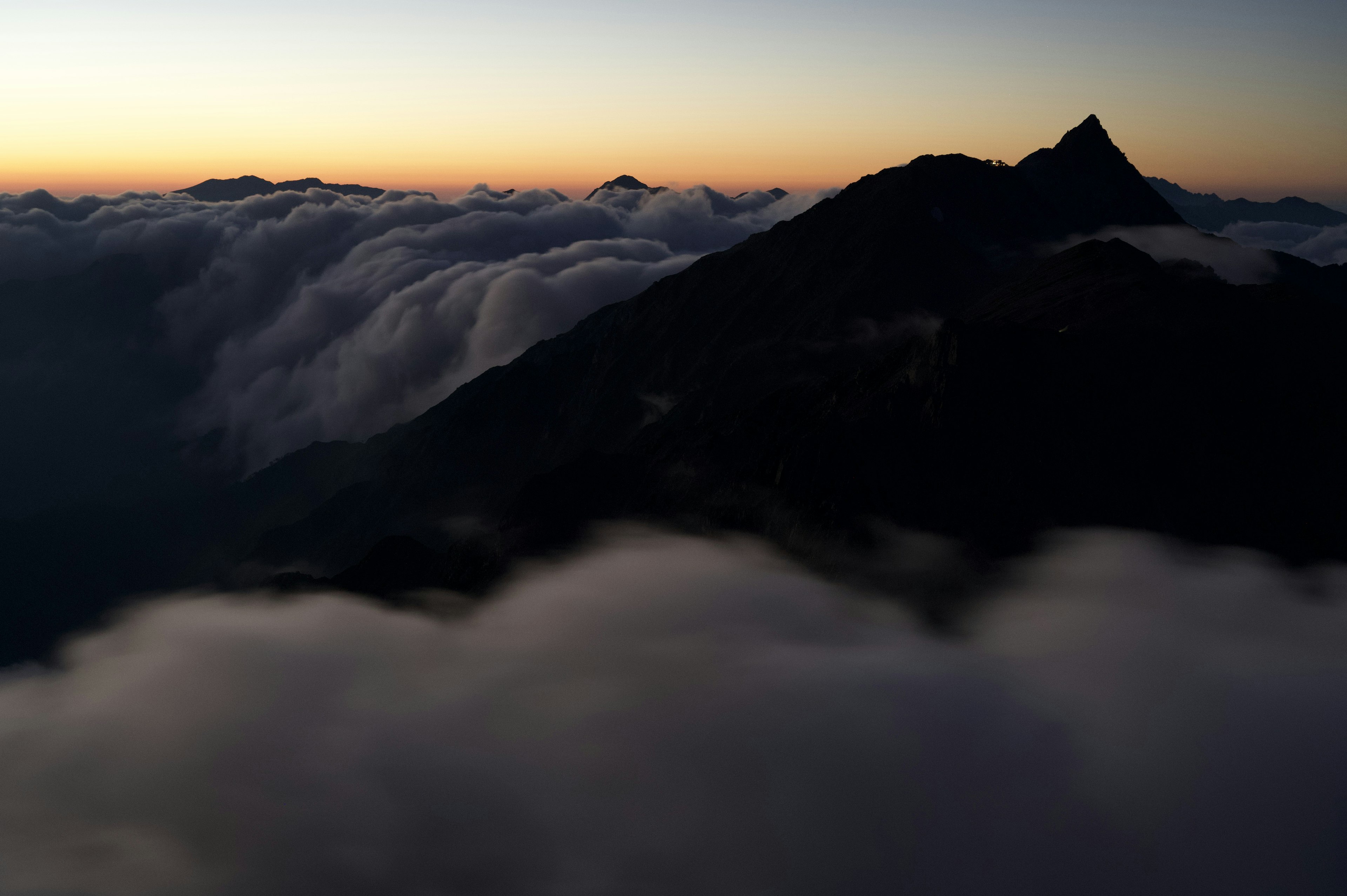 Silhouette eines Berges über einem Wolkenmeer mit einem Sonnenaufgangshimmel