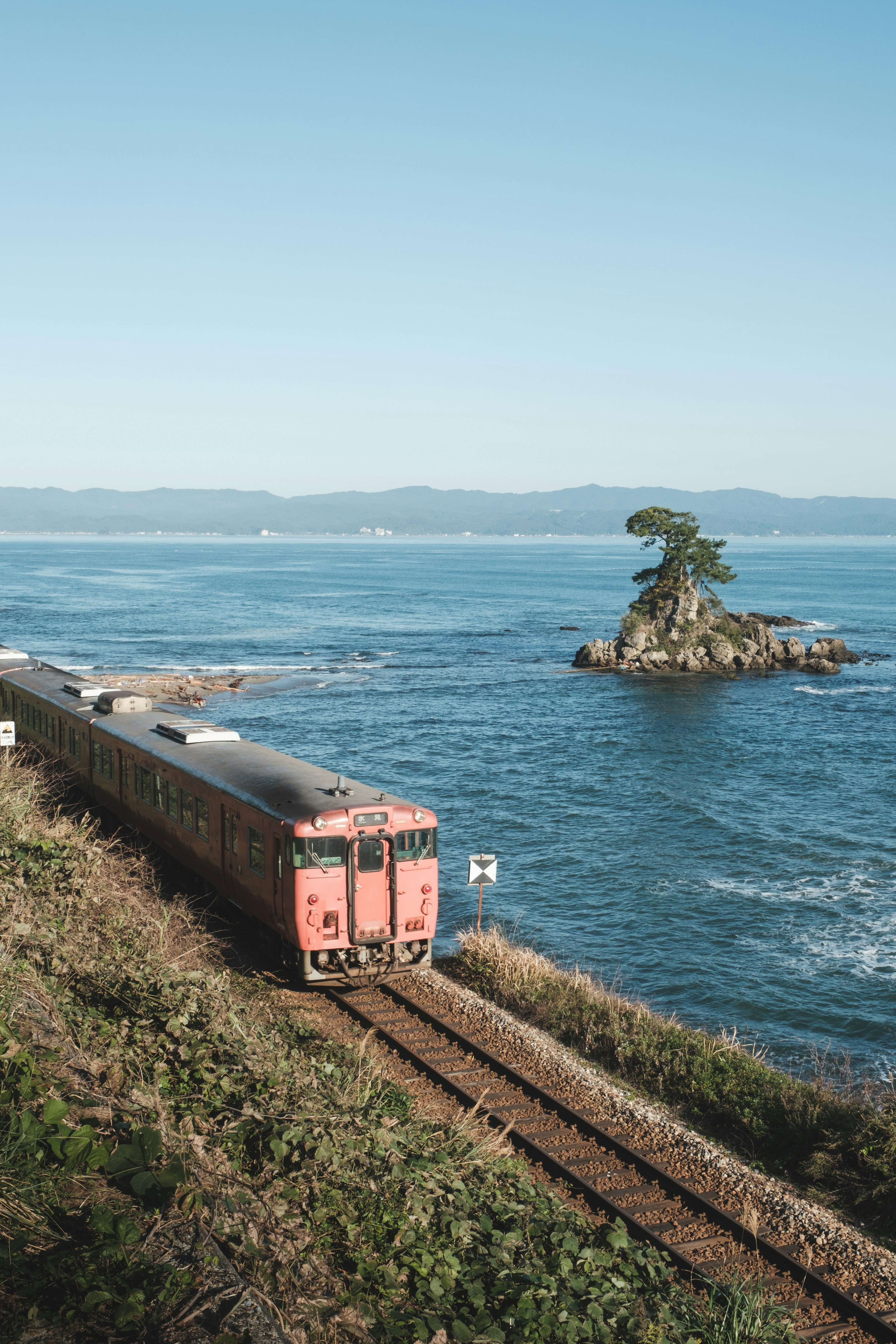 Scenic view of a train by the blue sea and a small island