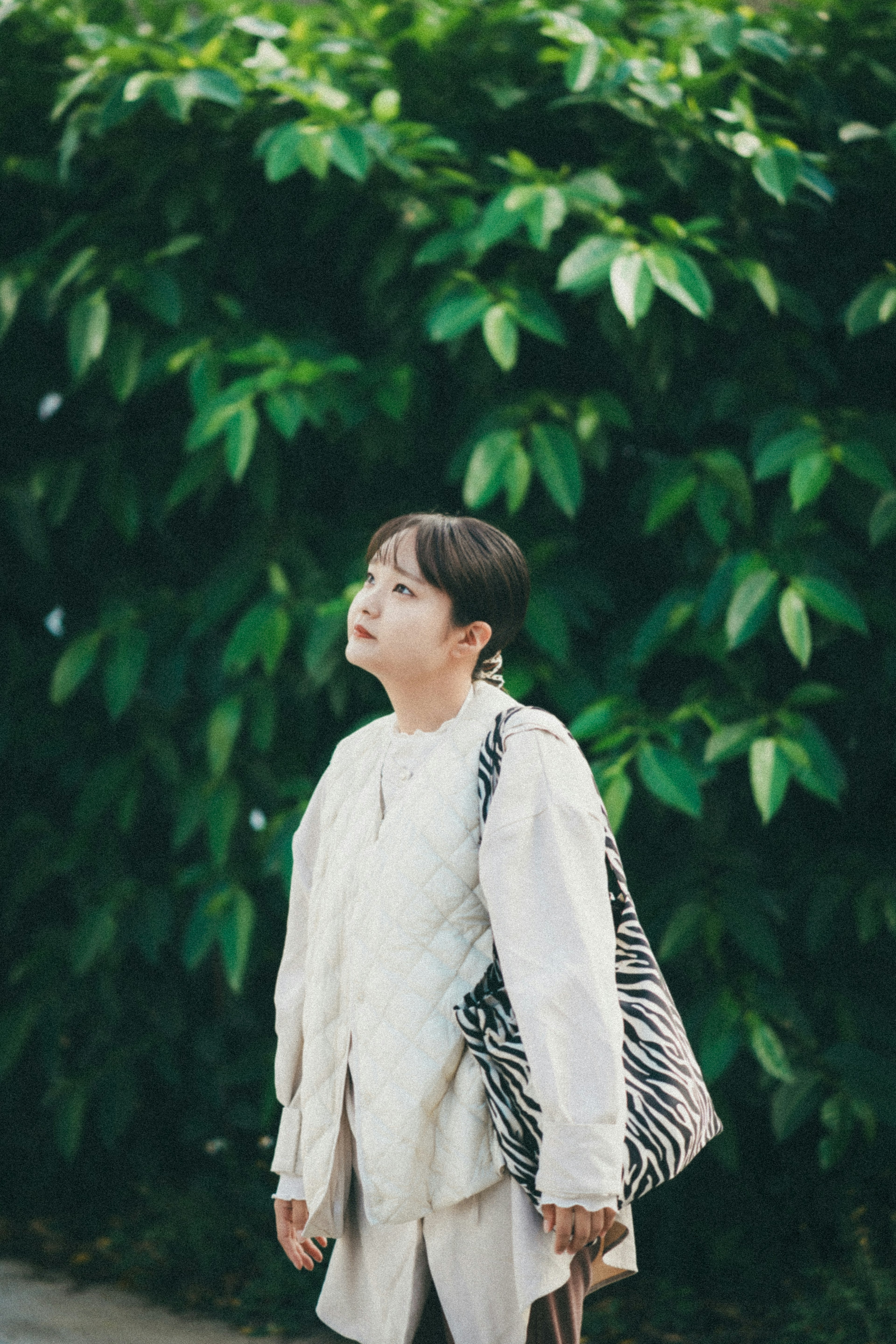 Person in white attire standing against a backdrop of green leaves