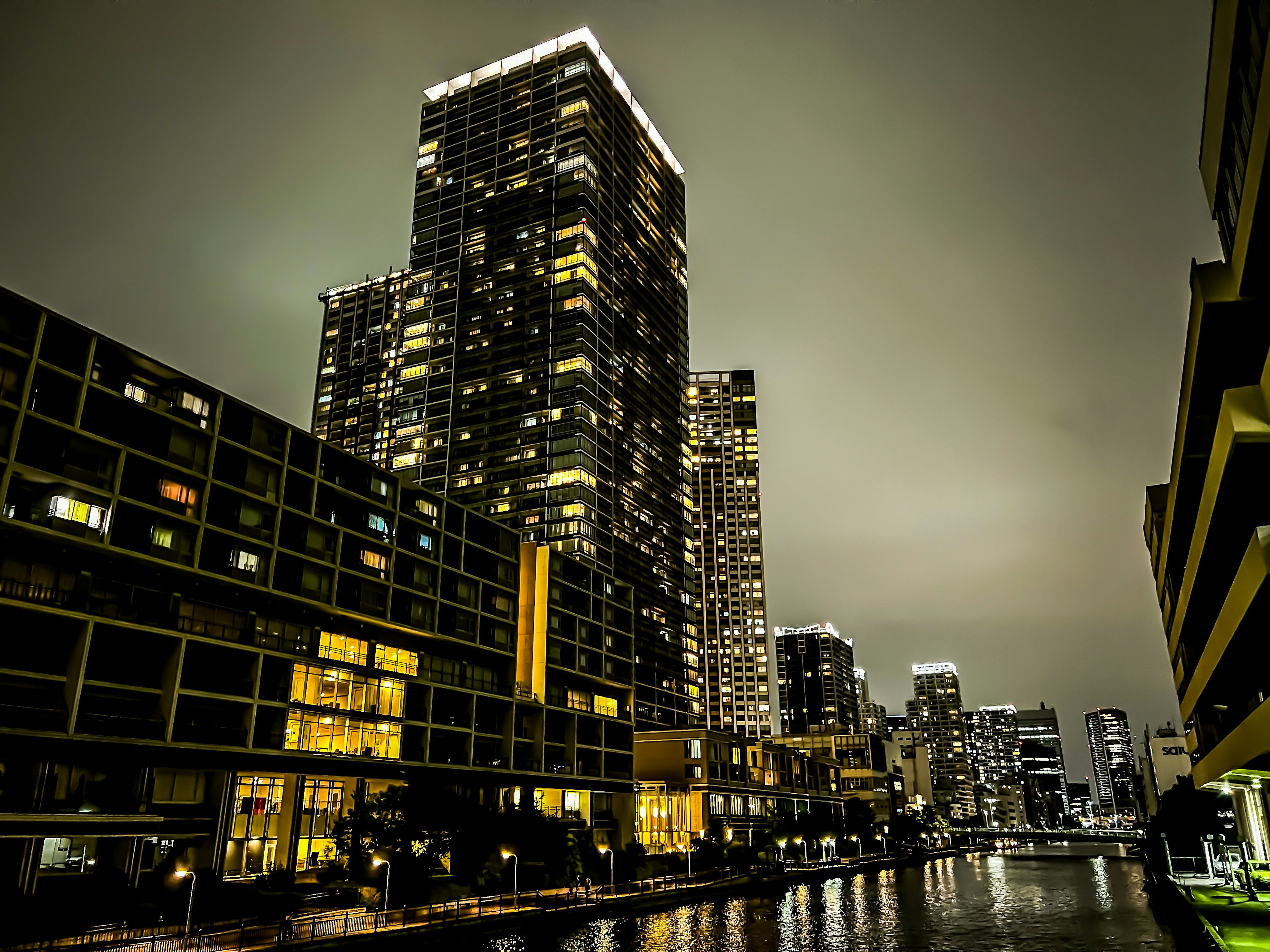 Night view along a river featuring tall buildings with illuminated windows