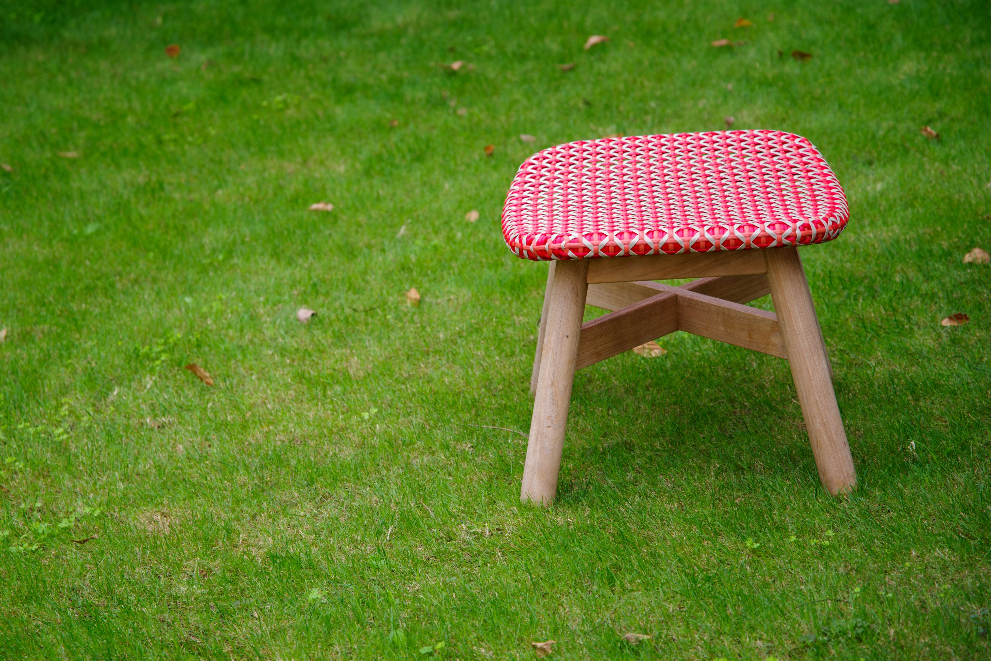 Kursi kayu dengan bantal kotak merah diletakkan di atas rumput hijau