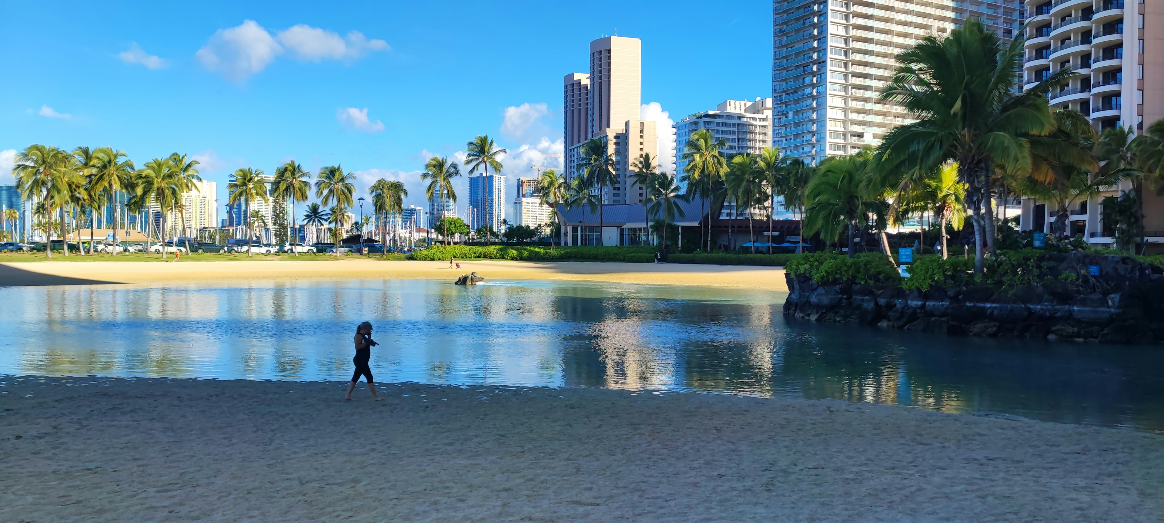 Scène de plage avec une personne marchant devant un ciel bleu et des gratte-ciels