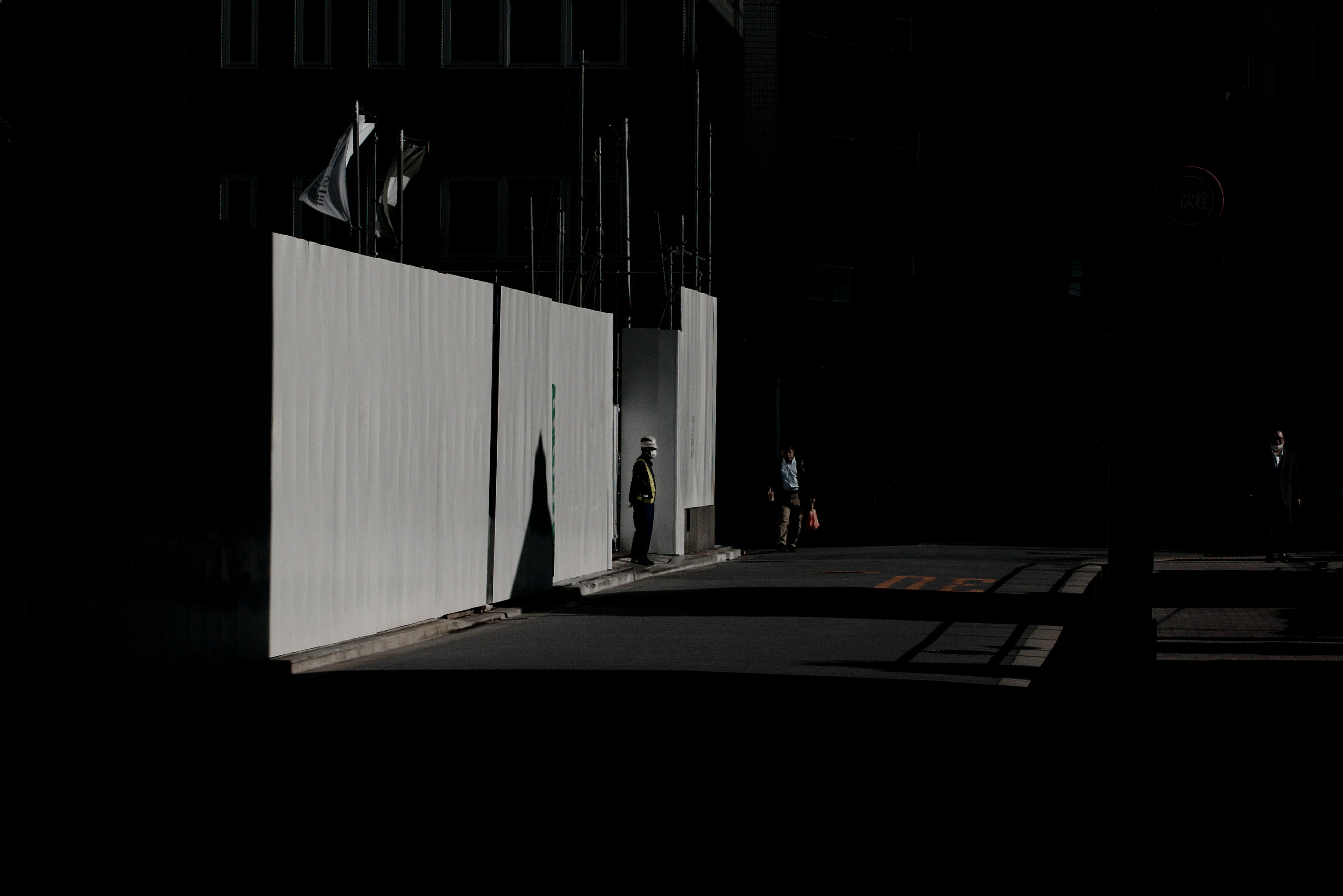 Scène urbaine avec un mur blanc et des silhouettes contre un fond sombre