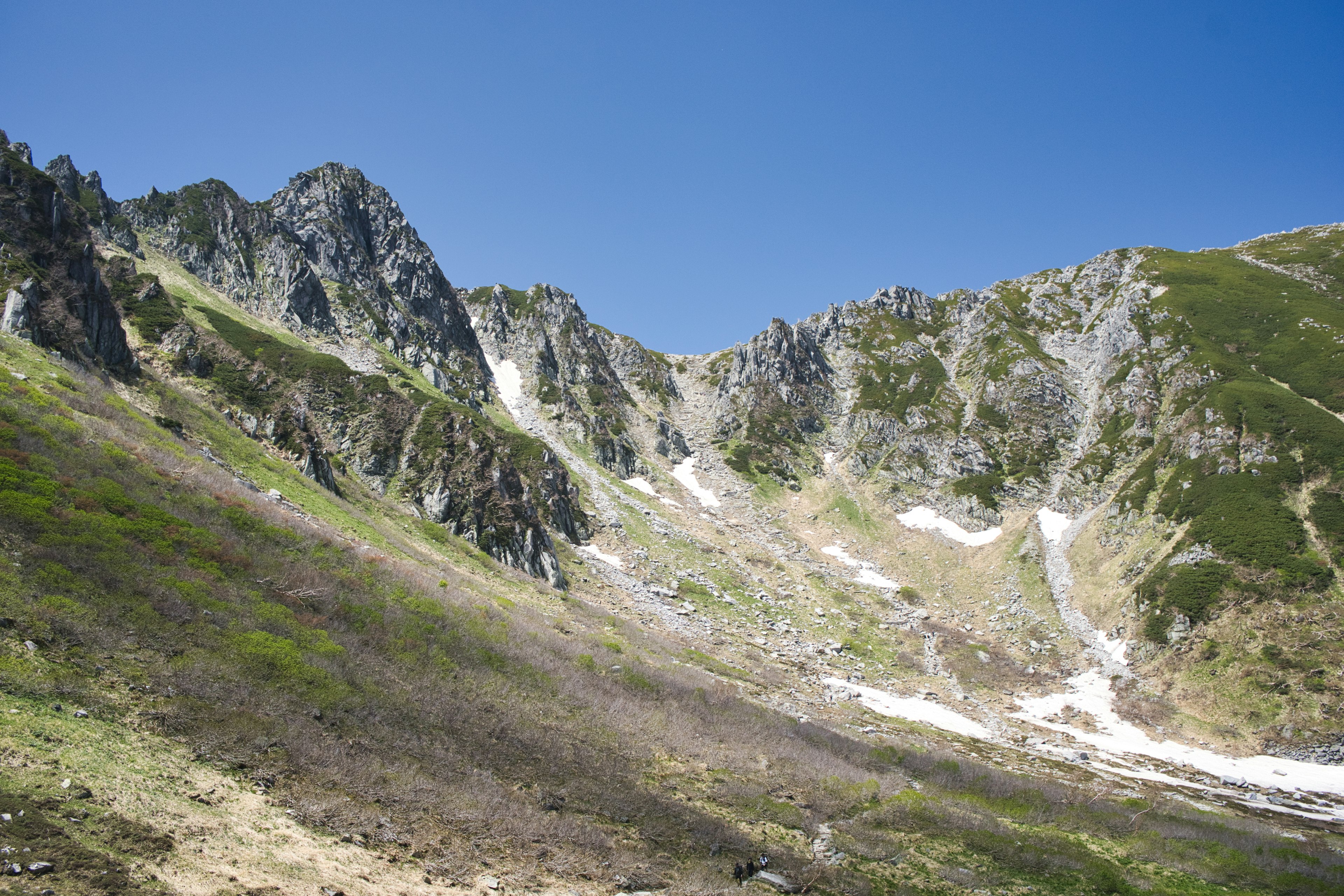 青空の下に広がる山の風景が見える岩だらけの斜面と緑の草地