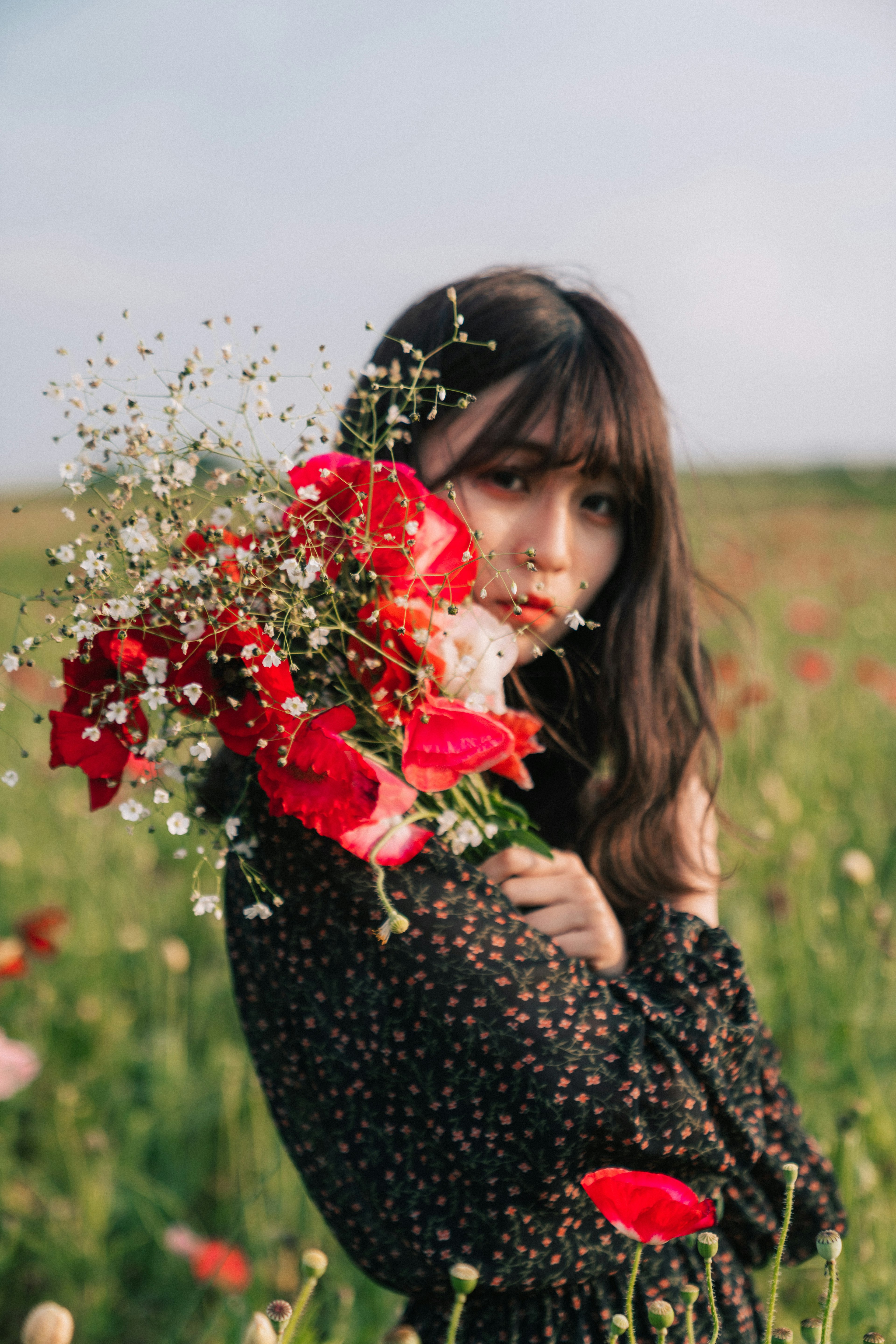 花束を持った女性が草原で微笑む情景