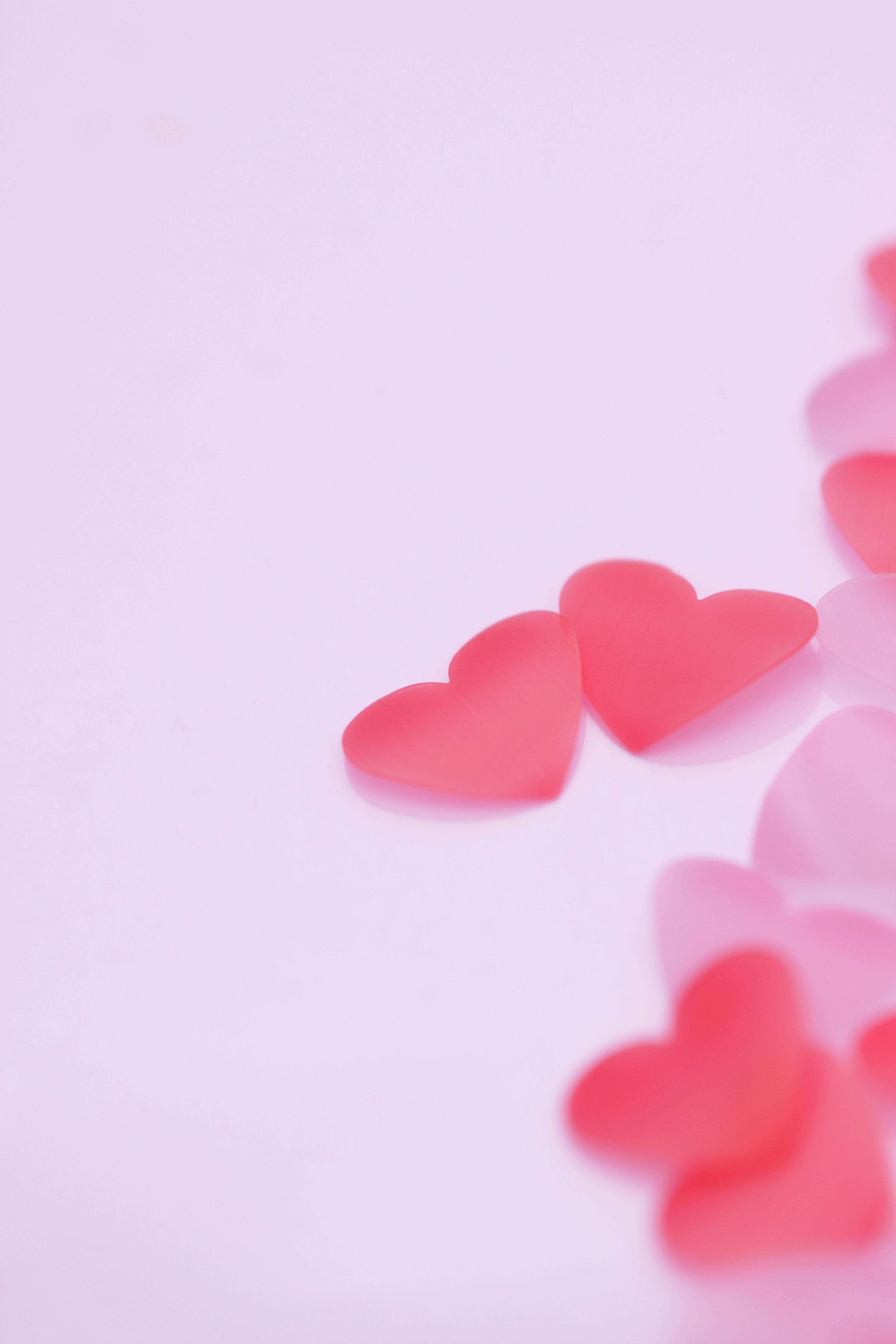 Decoraciones en forma de corazón rojas y rosa claro esparcidas sobre un fondo rosa claro