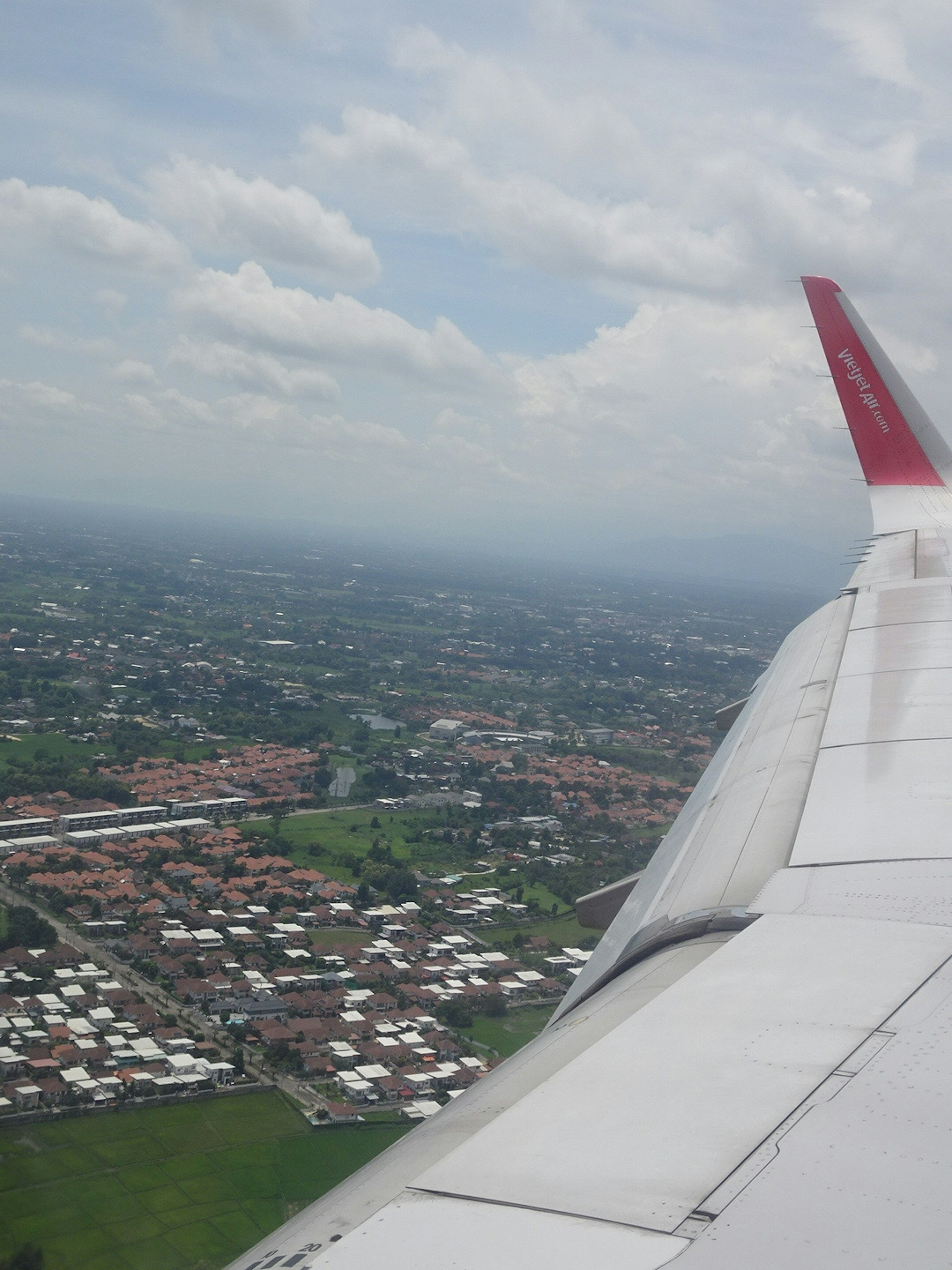 View from an airplane wing showing a city landscape with green areas and residential neighborhoods