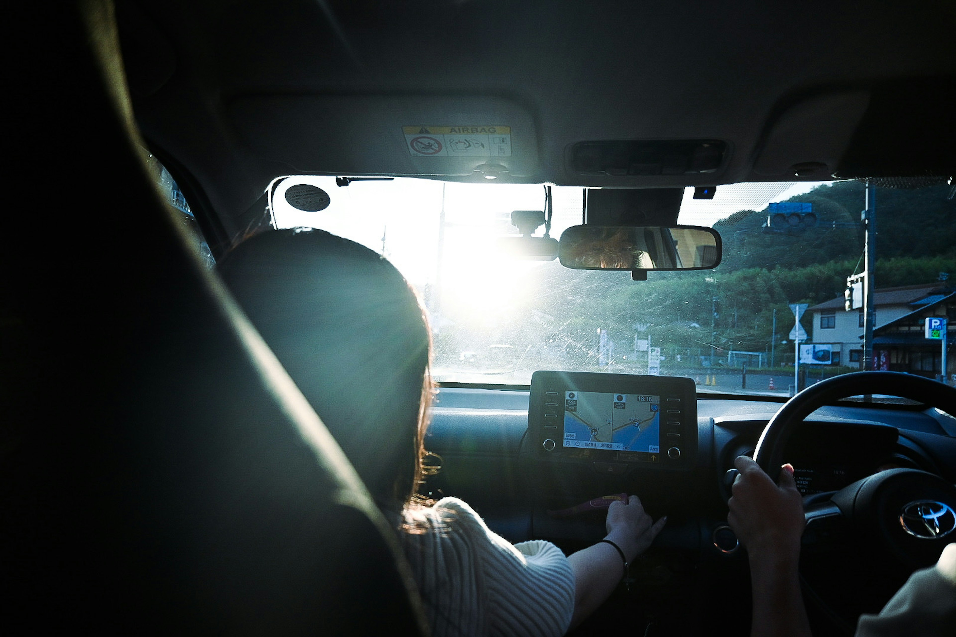 Una donna alla guida di un'auto con una luce solare brillante che entra dal parabrezza