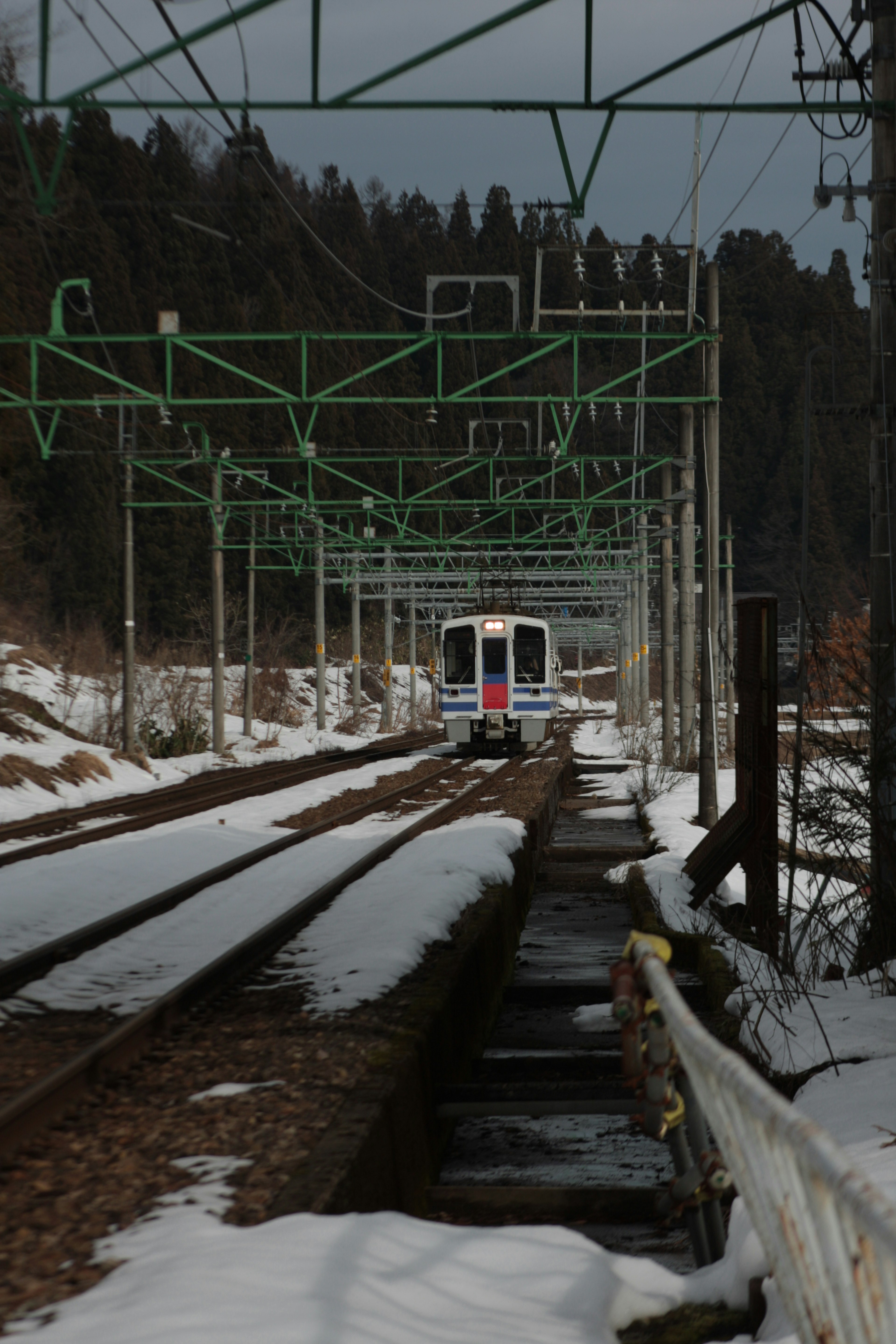 Train running on snowy railway under green overhead wires