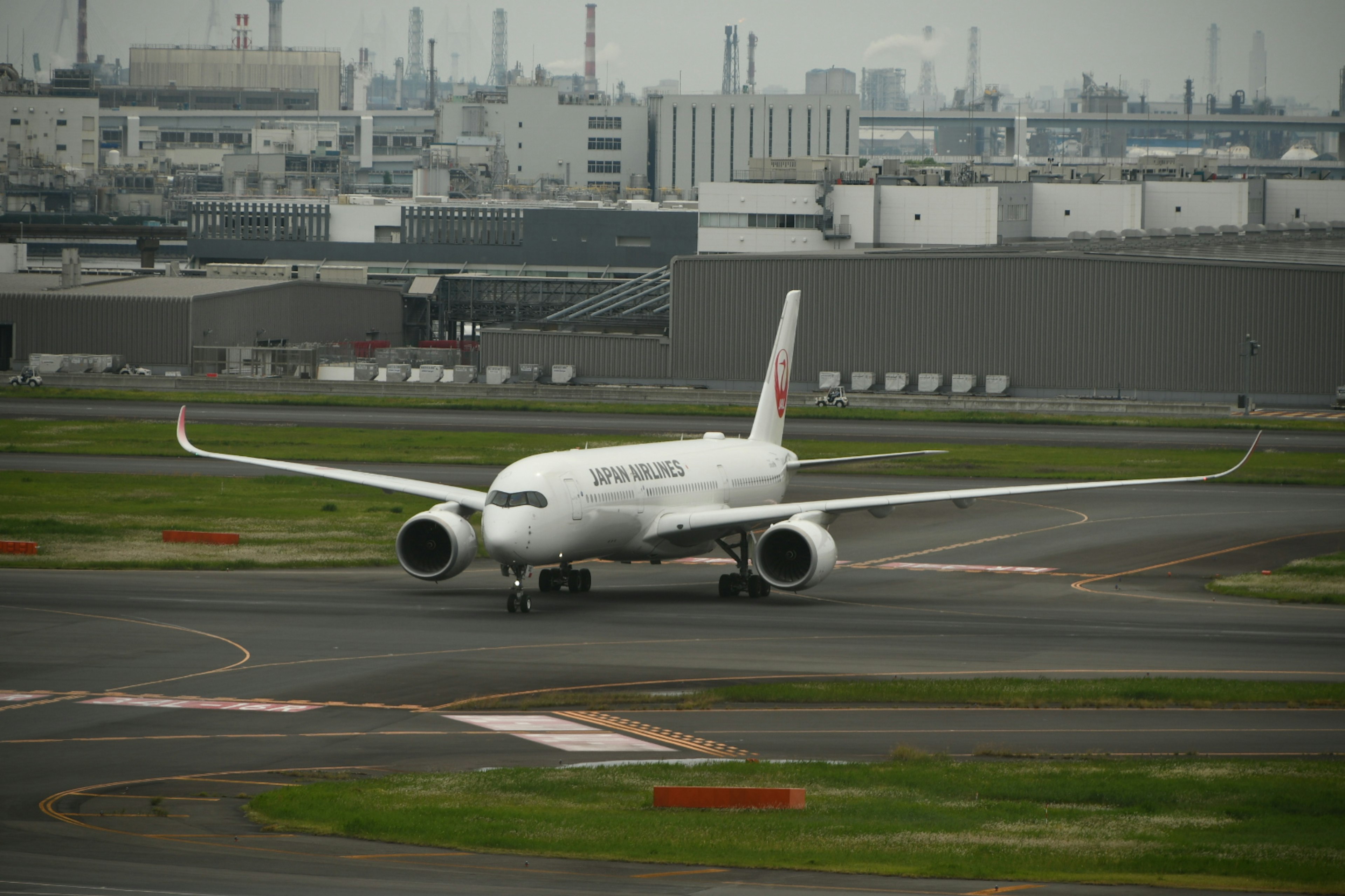 White airplane taxiing on a runway with an industrial background