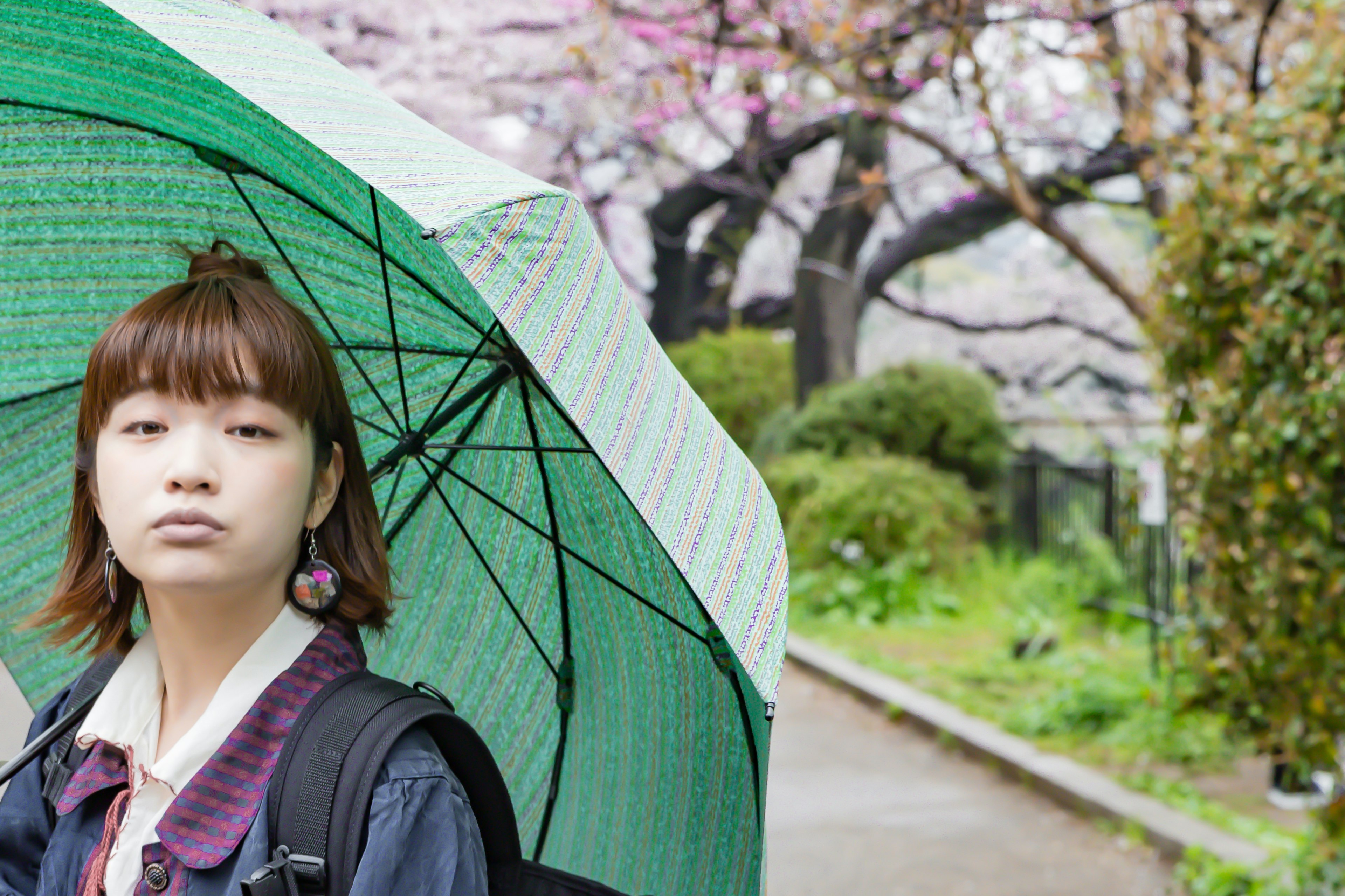 年輕女性拿著綠色雨傘站在公園裡，背景是櫻花