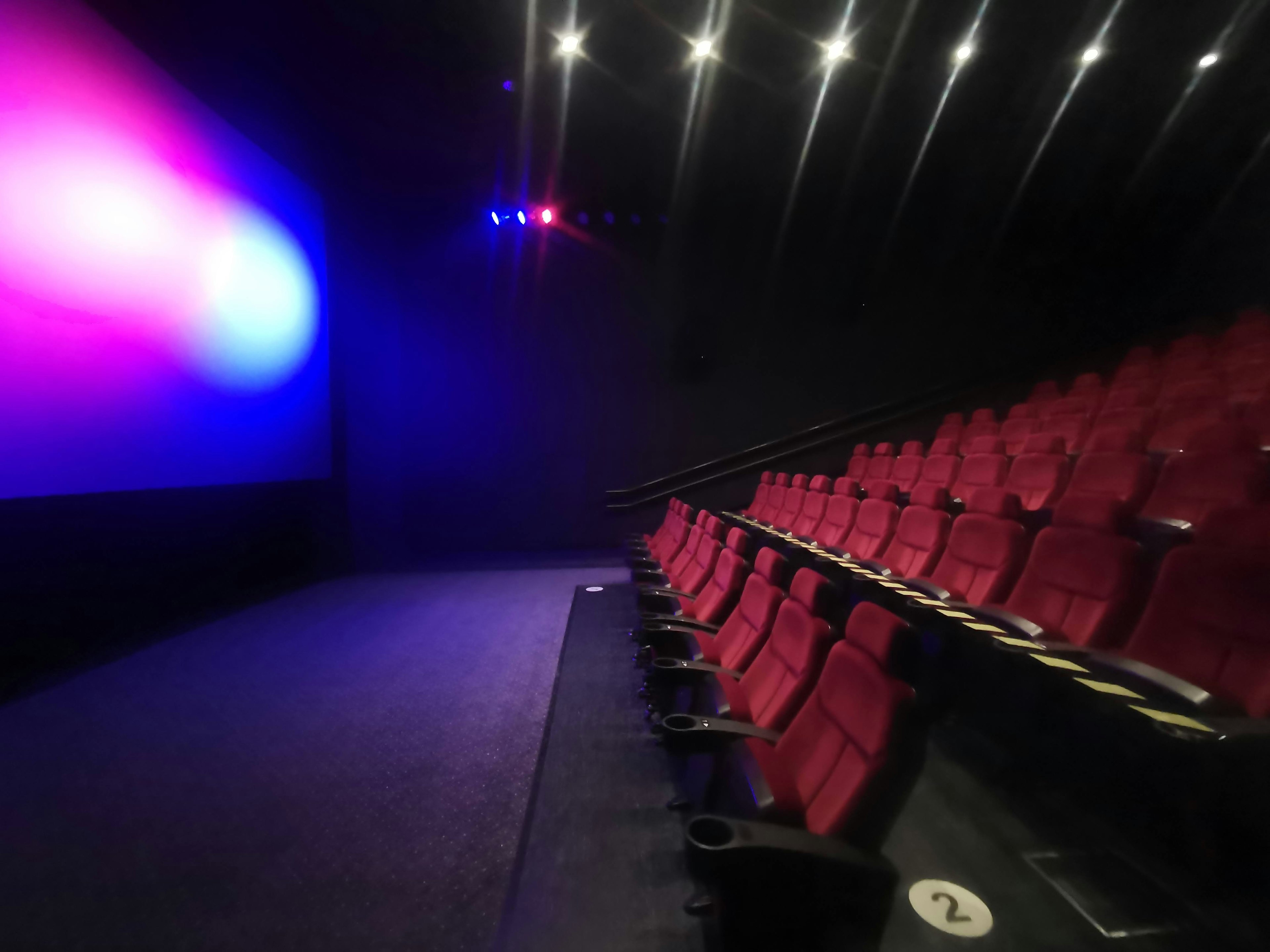 Cinema interior with red seats and dimly lit screen in blue and purple