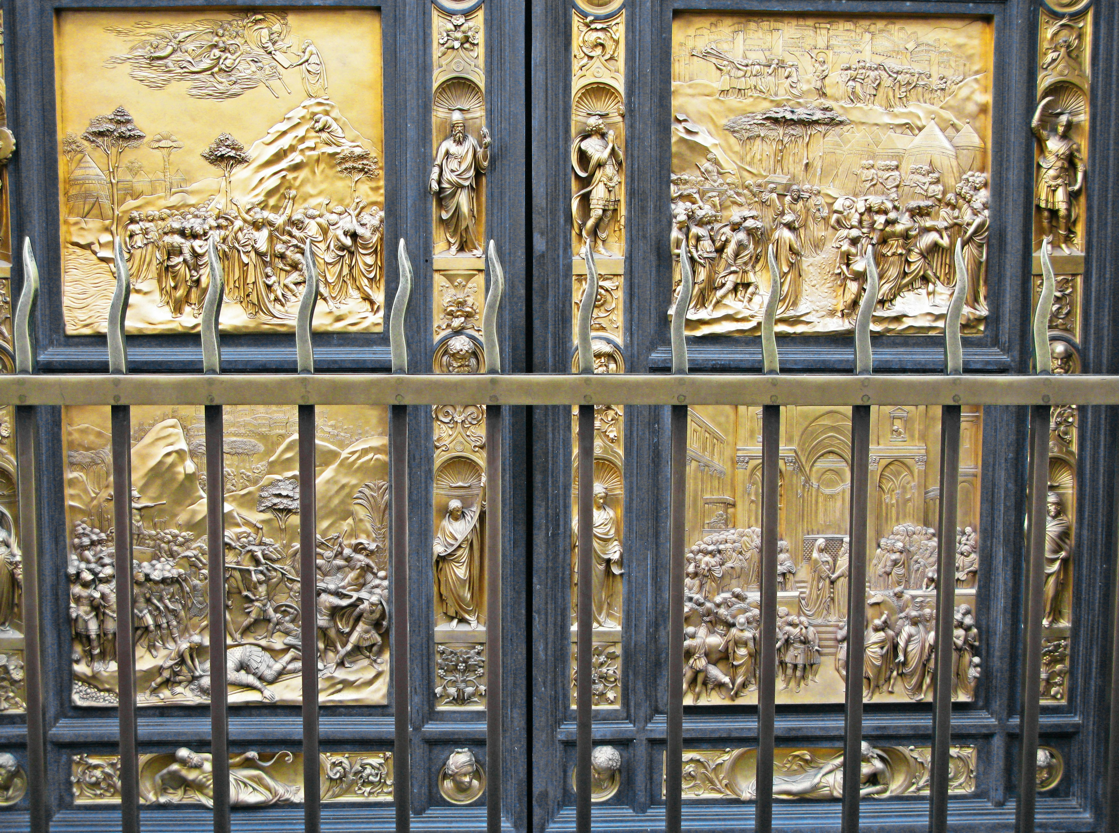 Detailed golden sculptures on doors with a metal fence