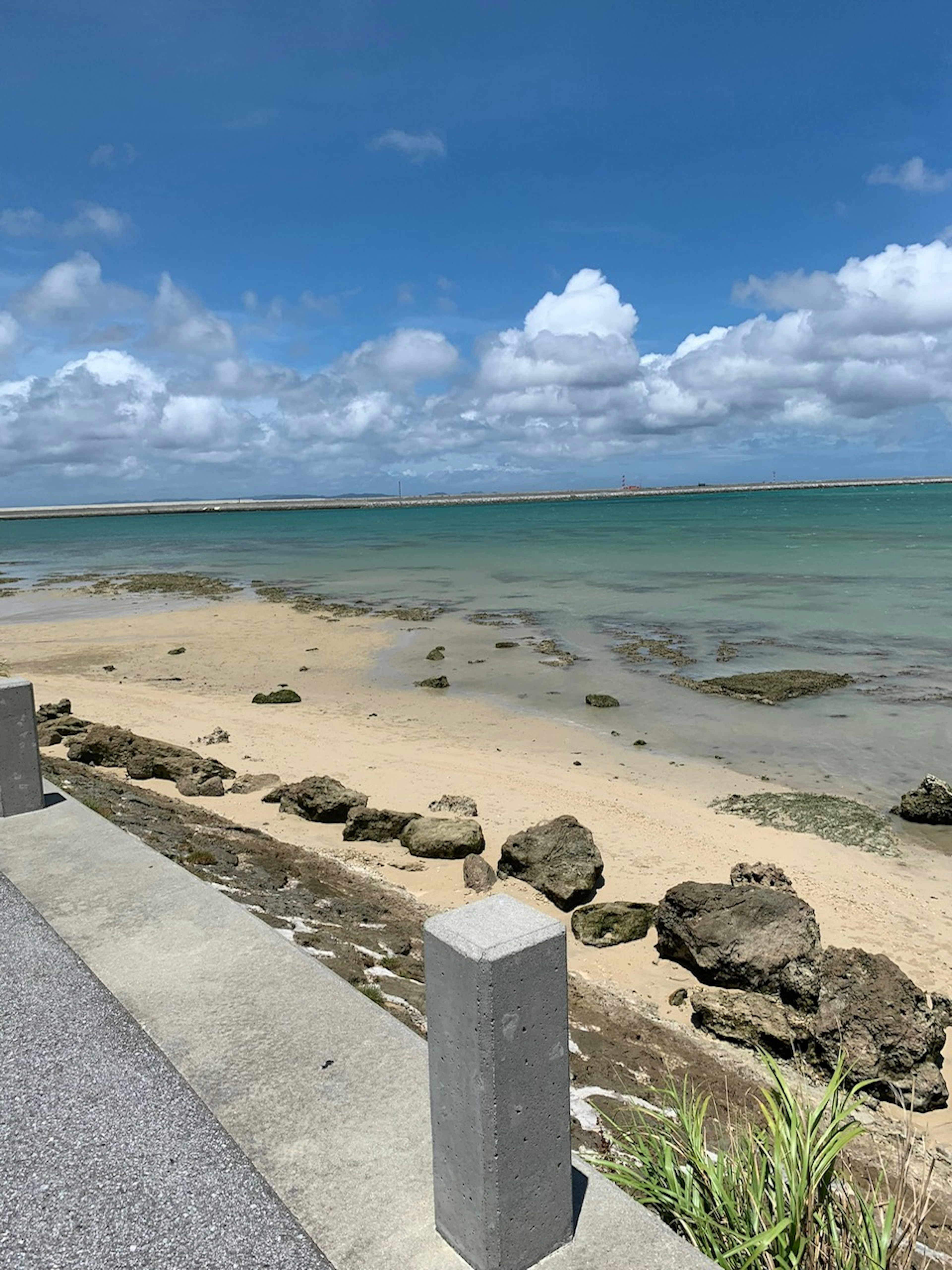 Beach landscape with blue sea and white clouds featuring rocks and sandy shore