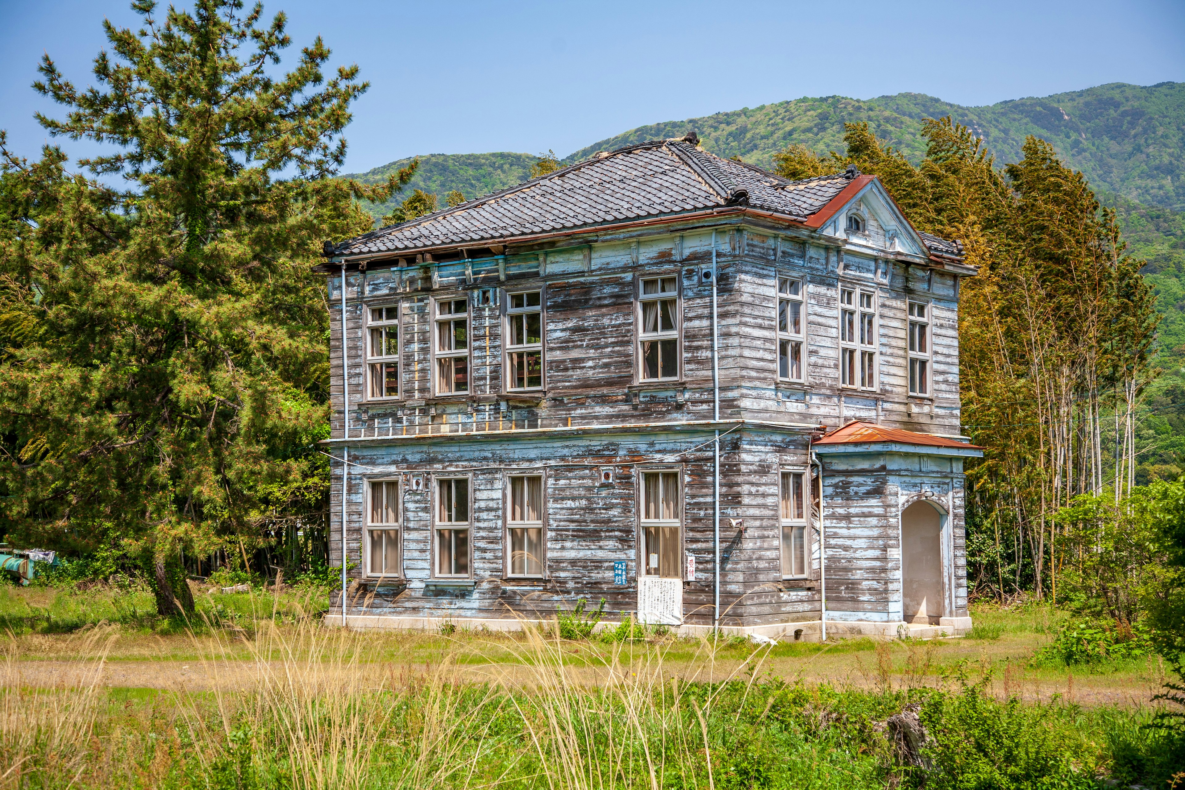 一座旧木建筑，蓝色油漆剥落，周围环绕着绿色植被