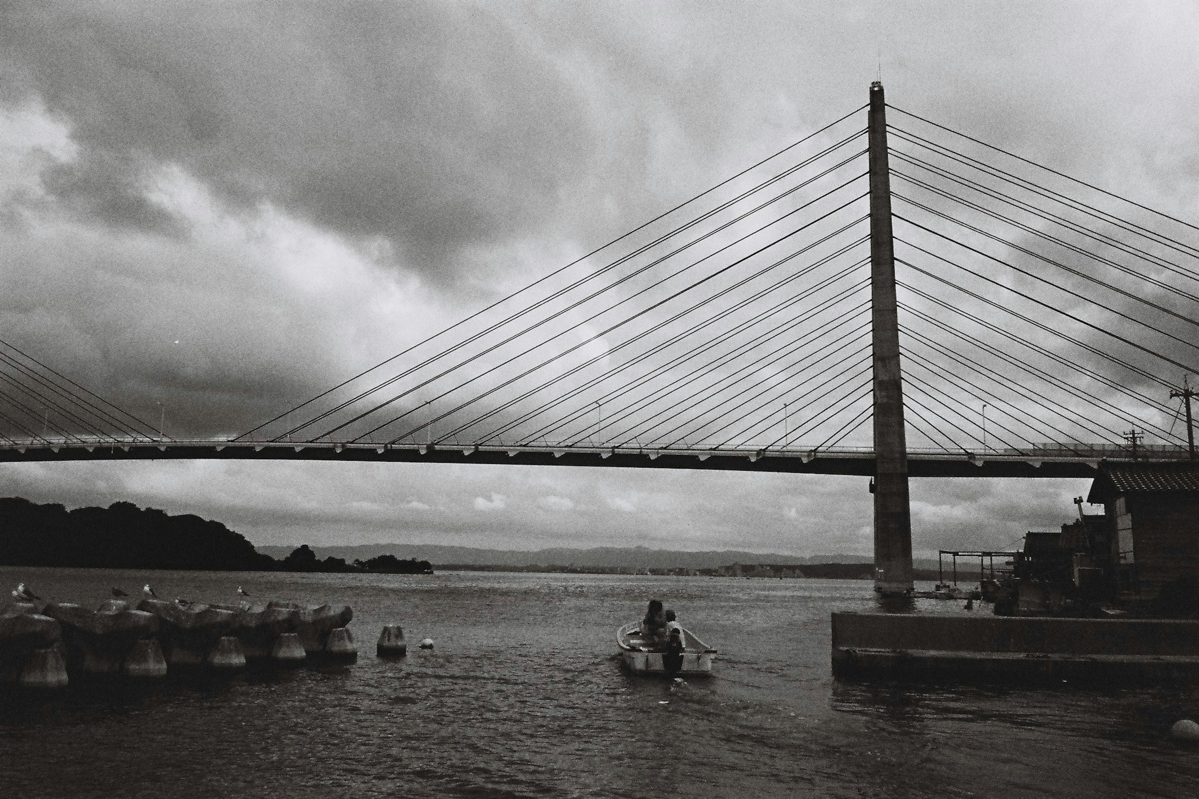 Image en noir et blanc d'un pont avec des câbles et de petits bateaux