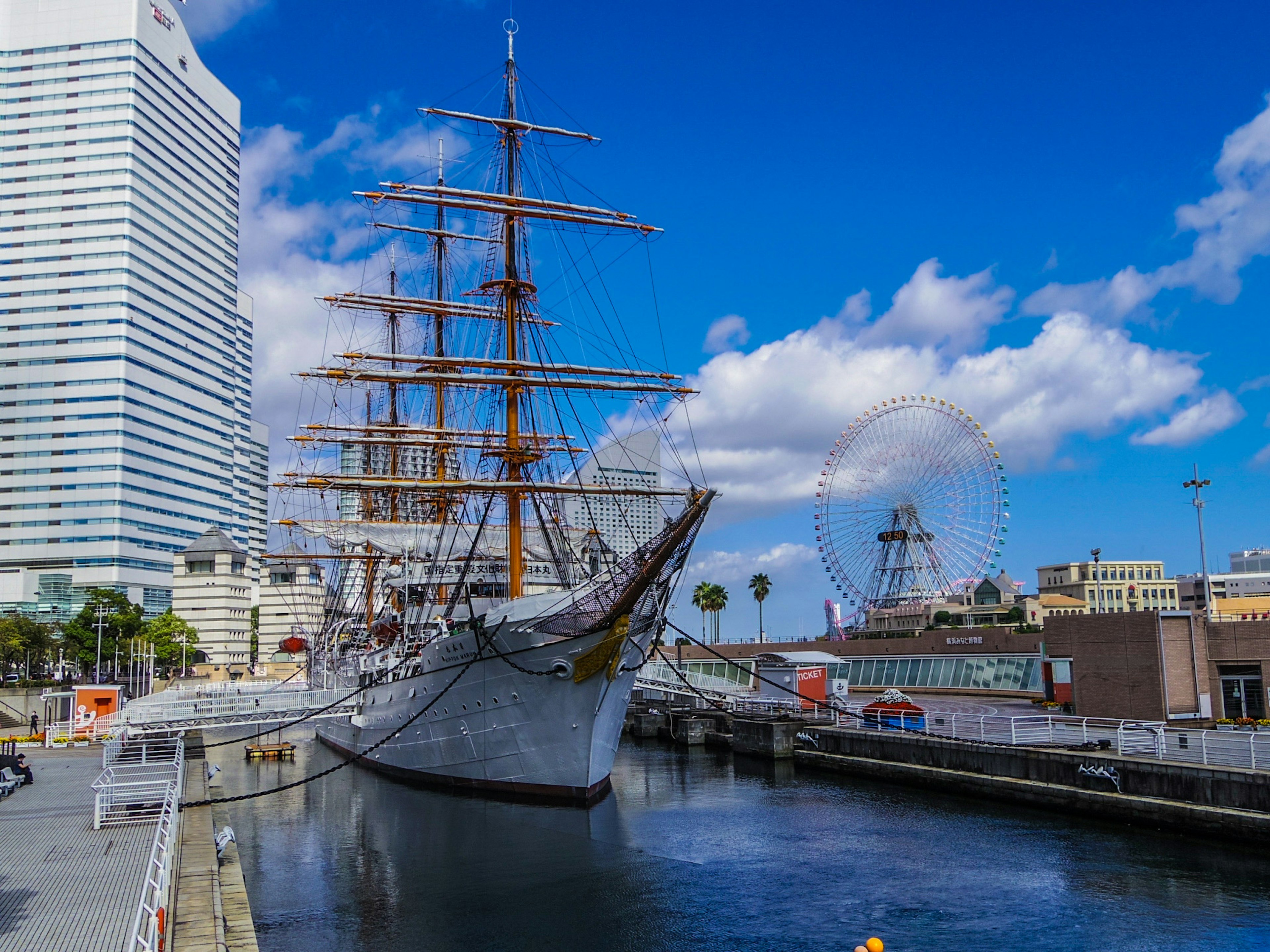 Un barco de vela atracado en el puerto de Yokohama con una noria cercana