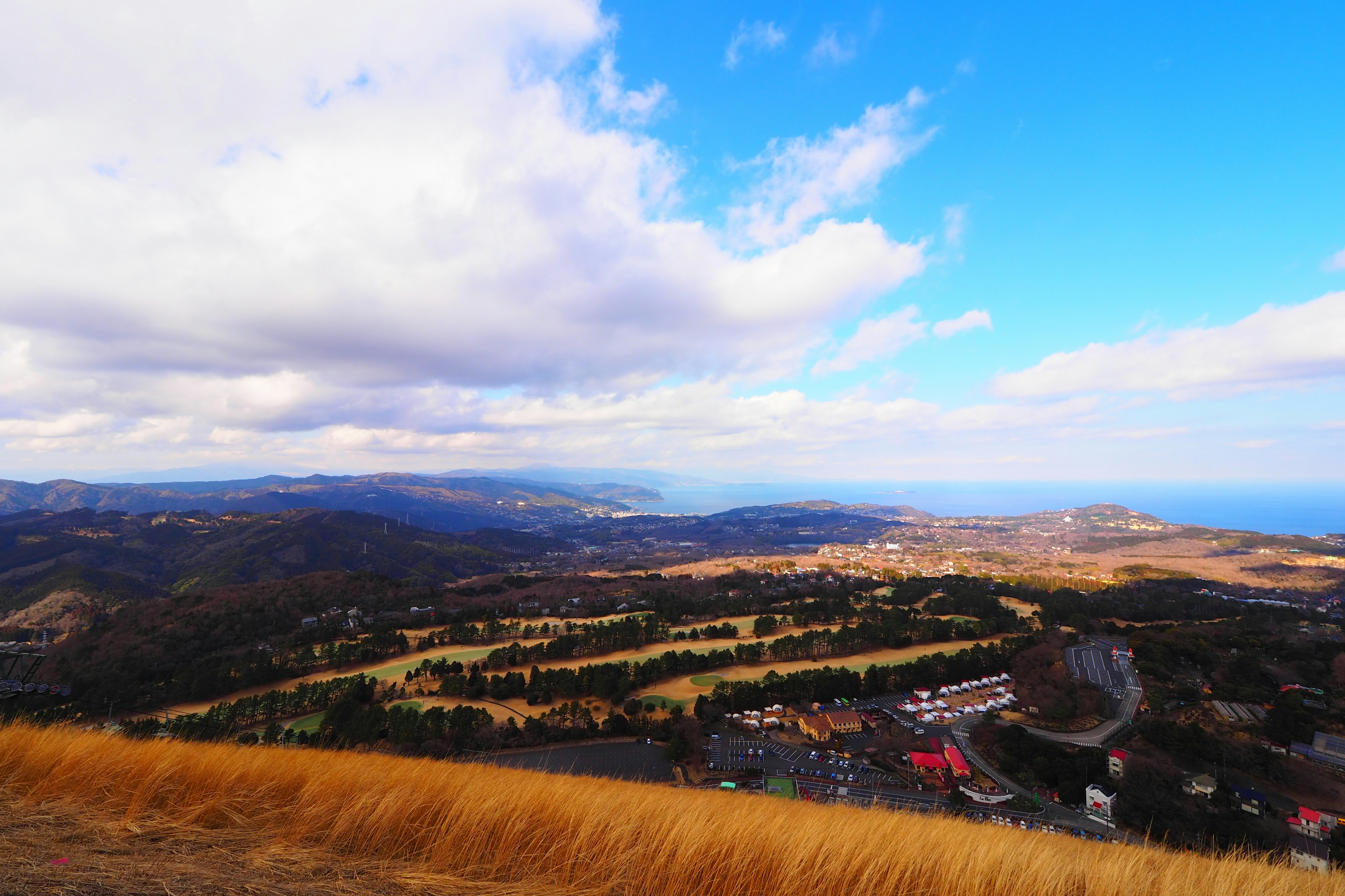 ทิวทัศน์ที่สวยงามของภูเขาใต้ท้องฟ้าสีฟ้าพร้อมก้อนเมฆ ทะเลที่มองเห็นได้จากระยะไกล ทุ่งหญ้าและพื้นที่ที่อยู่อาศัยด้านล่าง