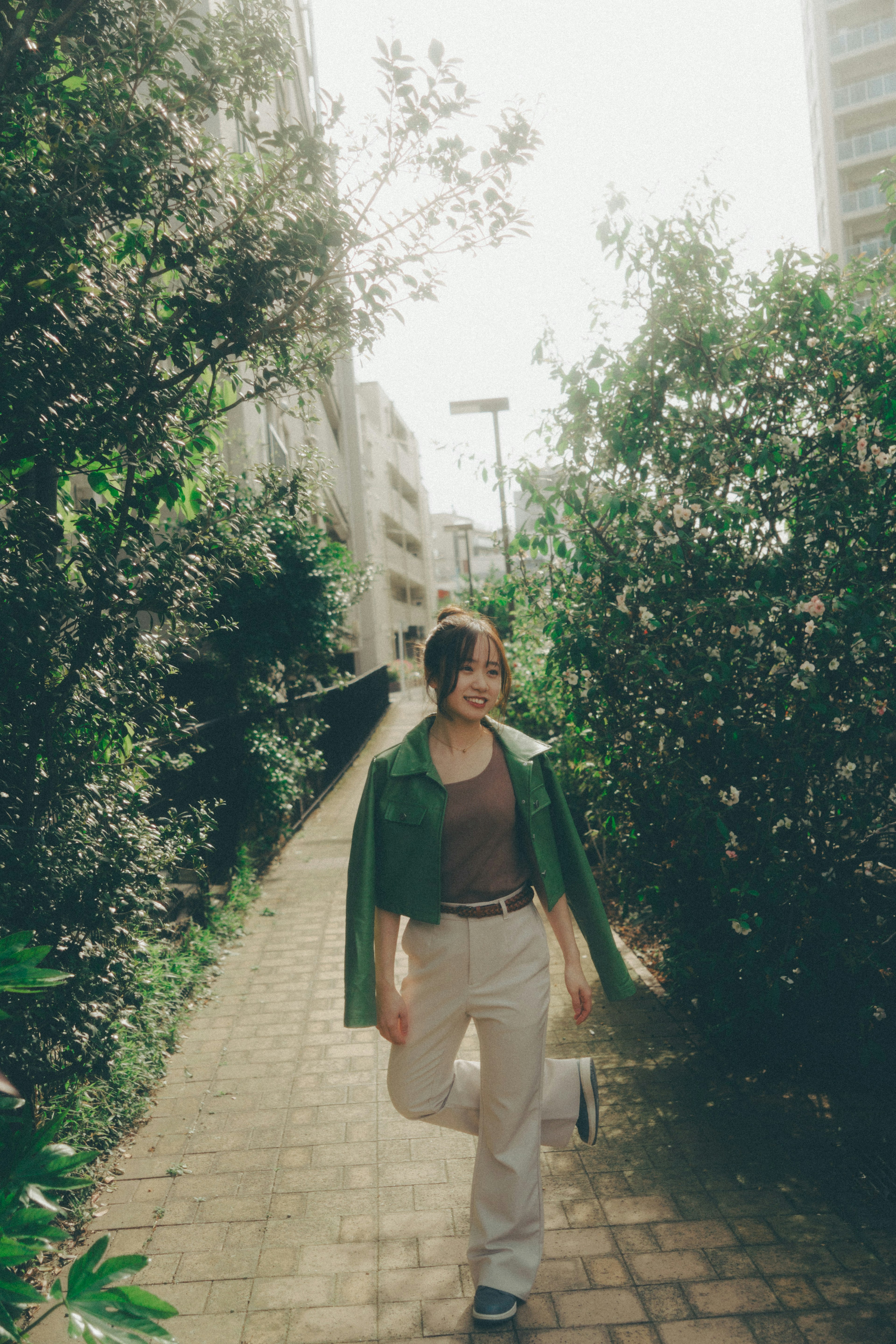 Woman in green jacket walking along a flower-lined pathway