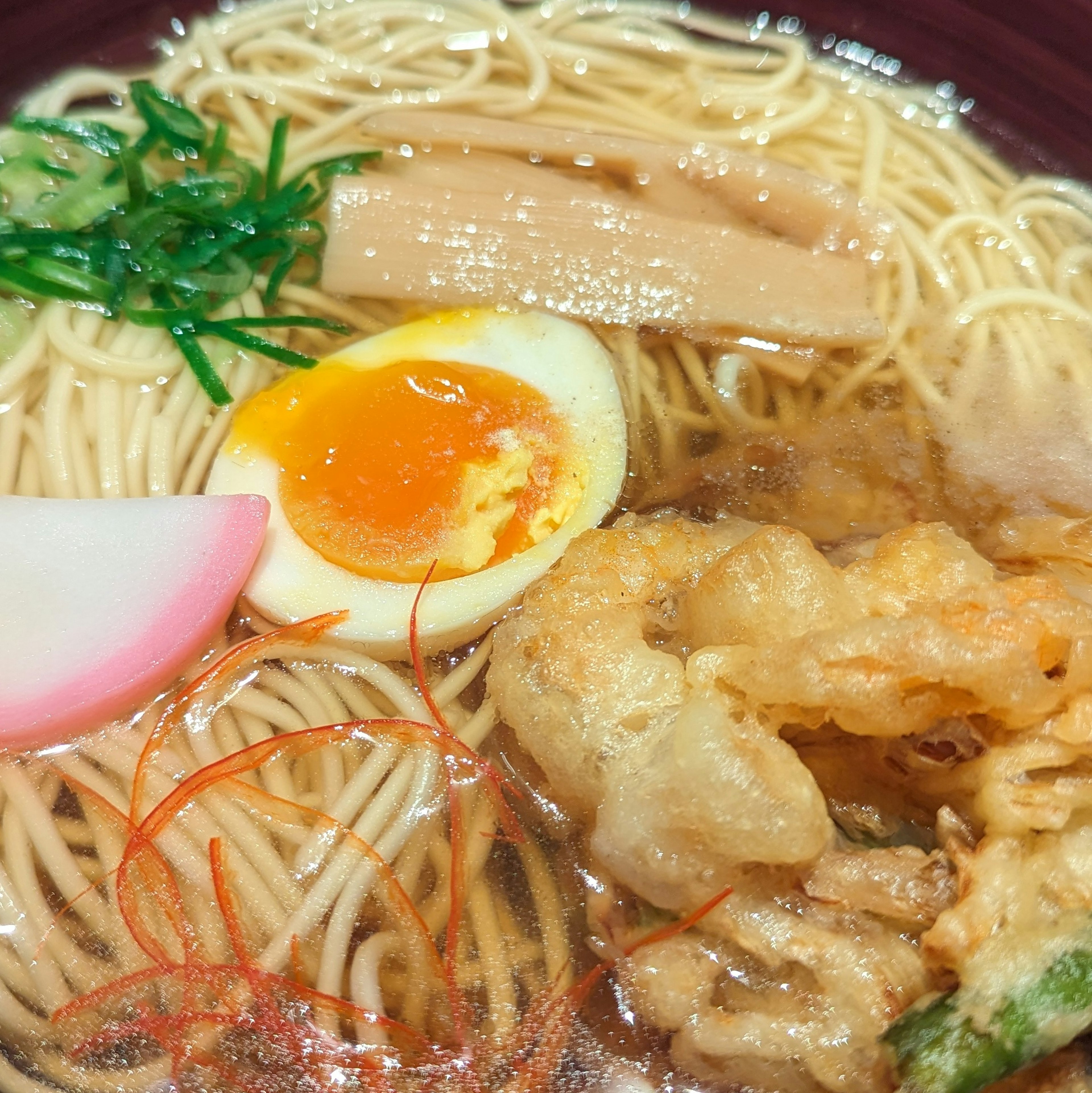 A delicious bowl of ramen topped with soft-boiled egg, tempura, green onions, menma, and kamaboko