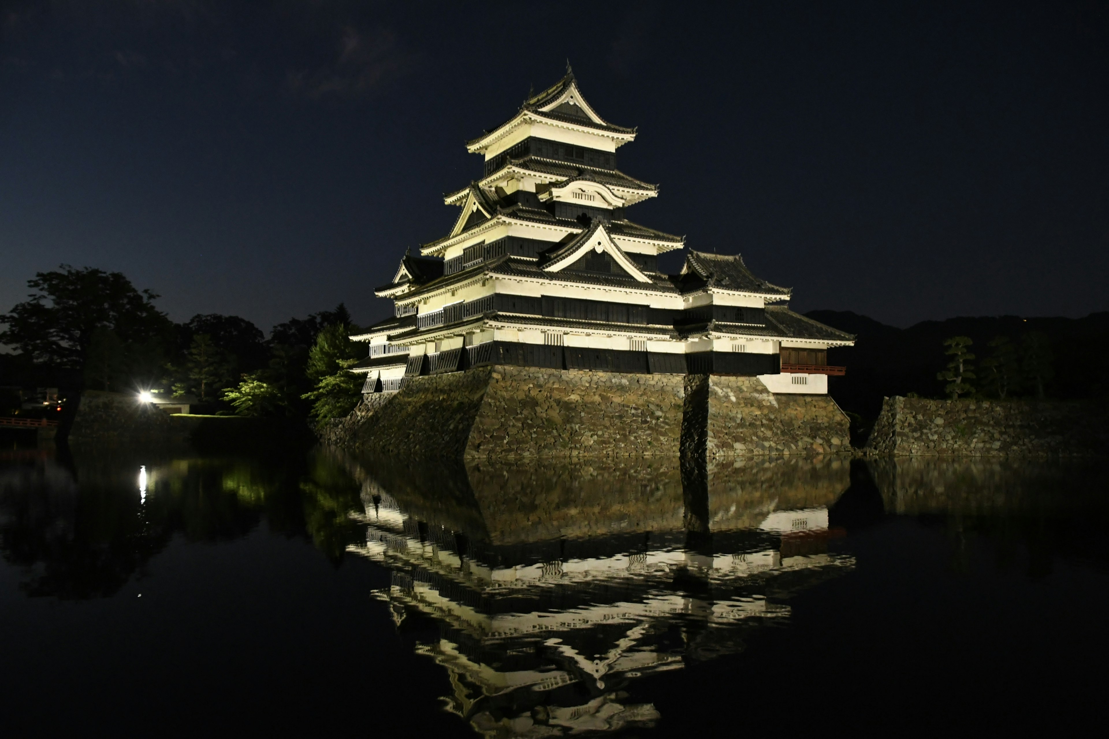 Castello di Matsumoto illuminato di notte che si riflette nell'acqua