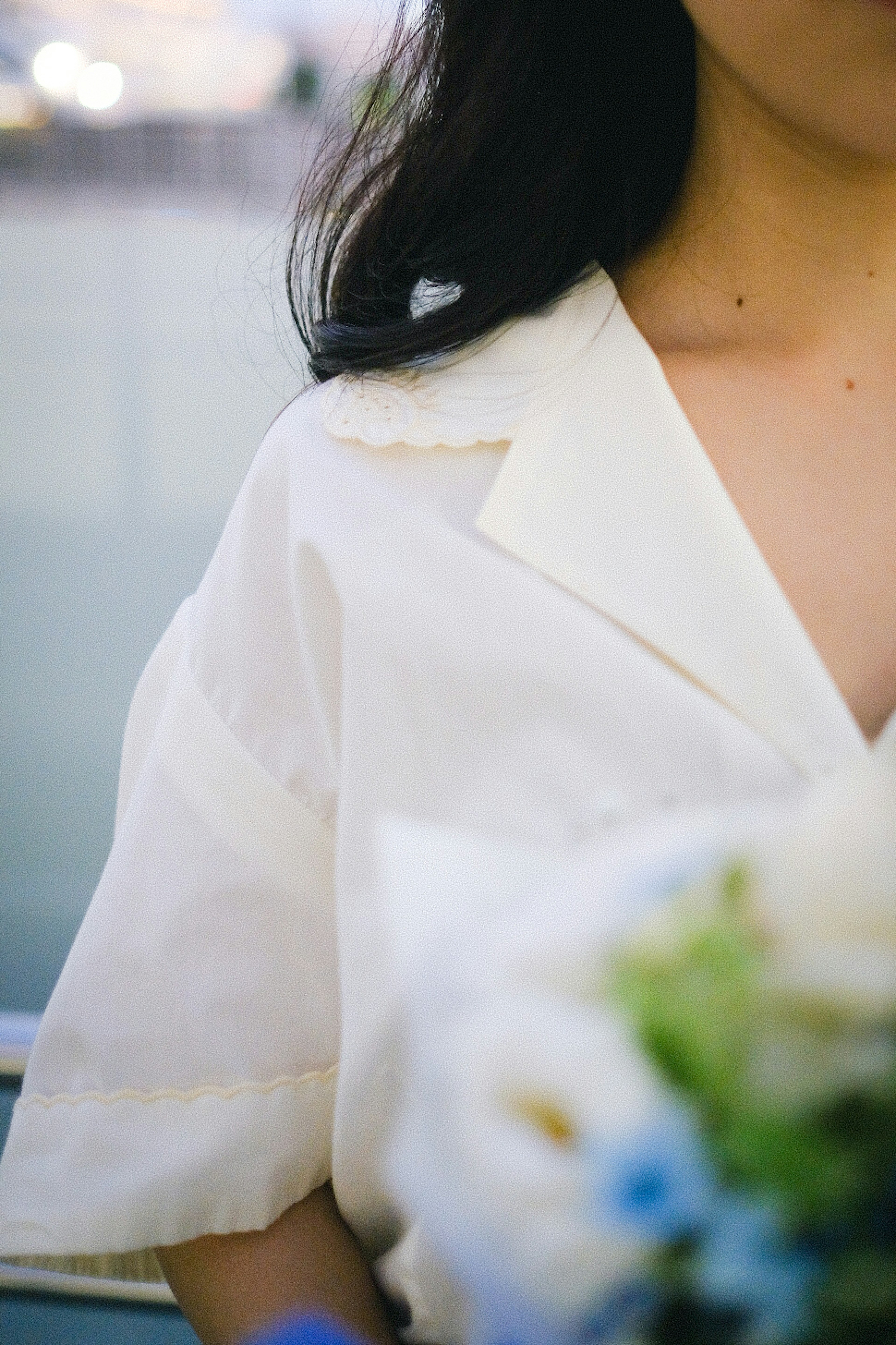 Spalla di una donna con camicia bianca che tiene un bouquet di fiori