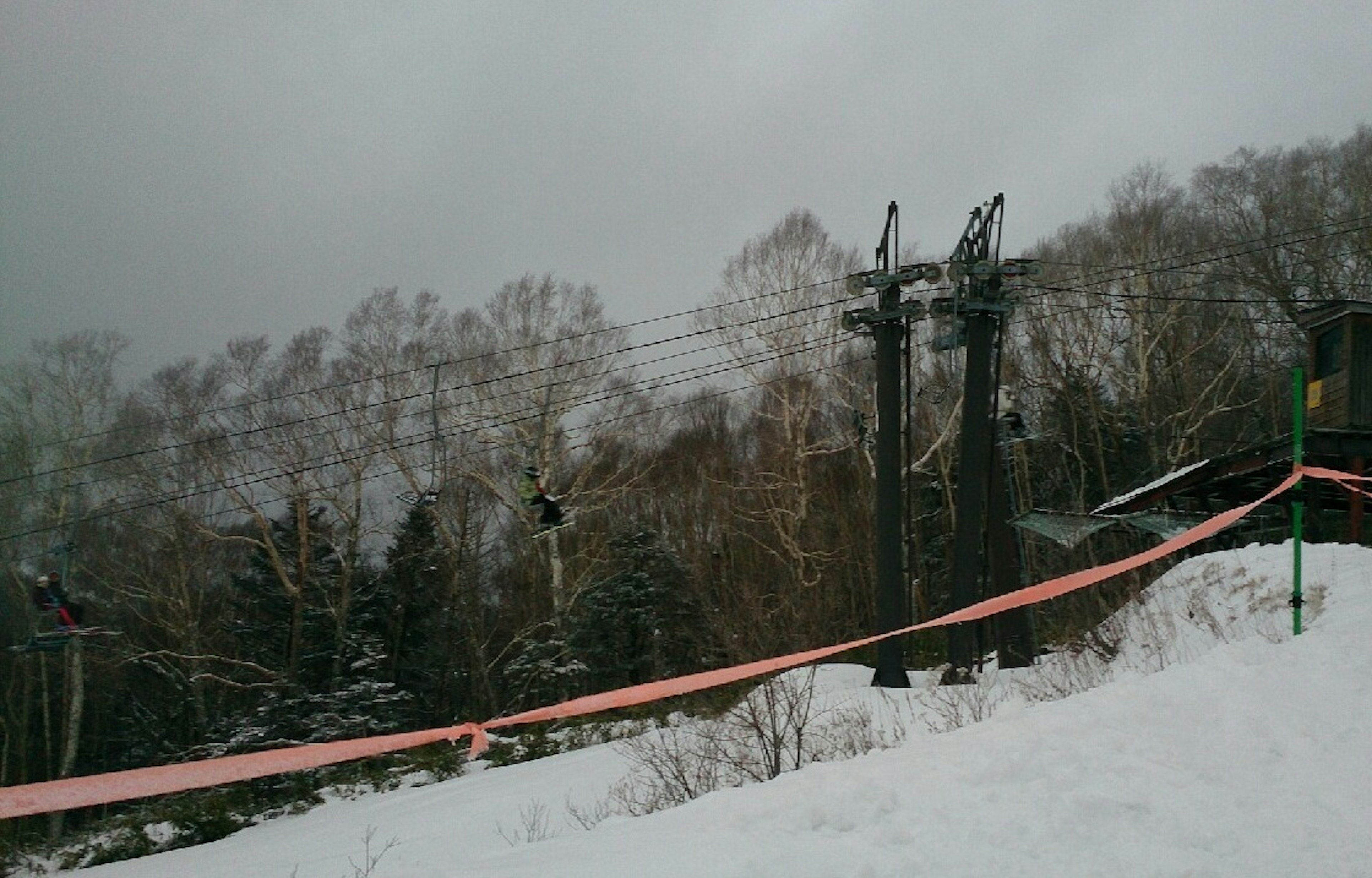 雪に覆われた山の斜面にあるリフトの支柱が見える曇りの日の風景