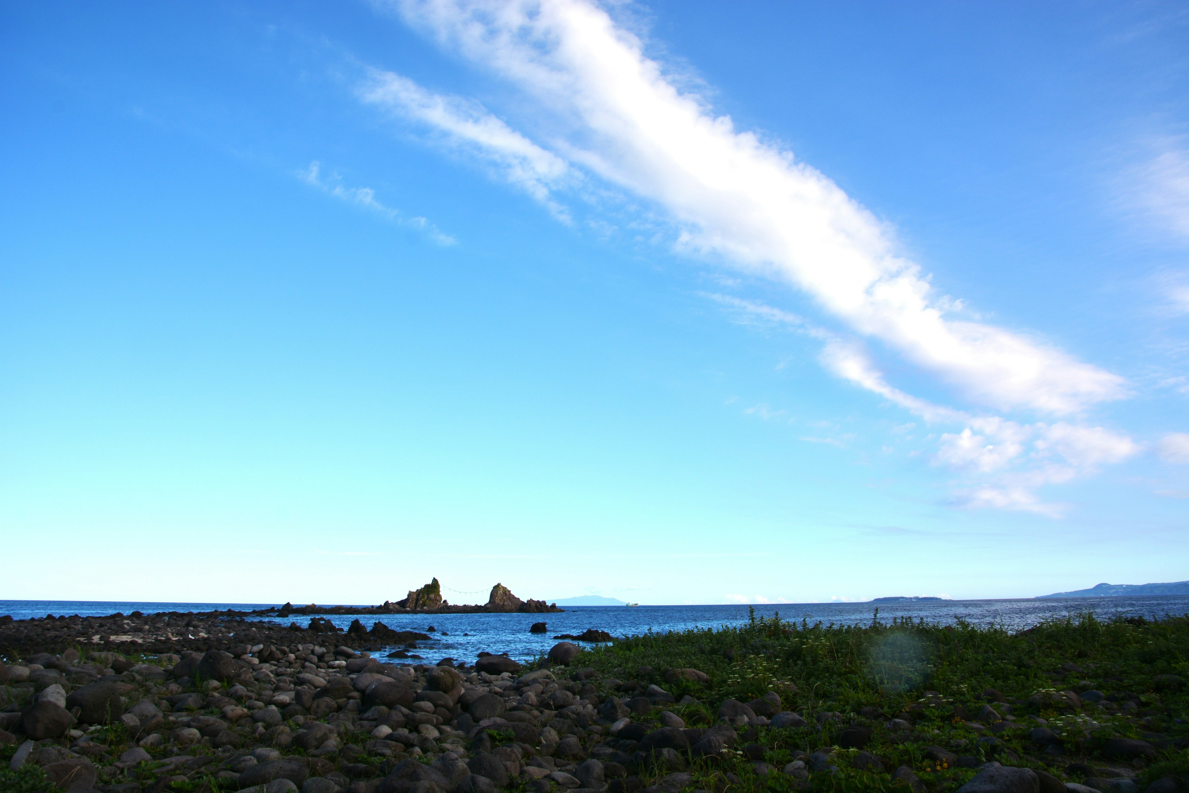 Küstenlandschaft mit blauem Himmel und Wolken sowie felsigem Ufer und grünem Gras