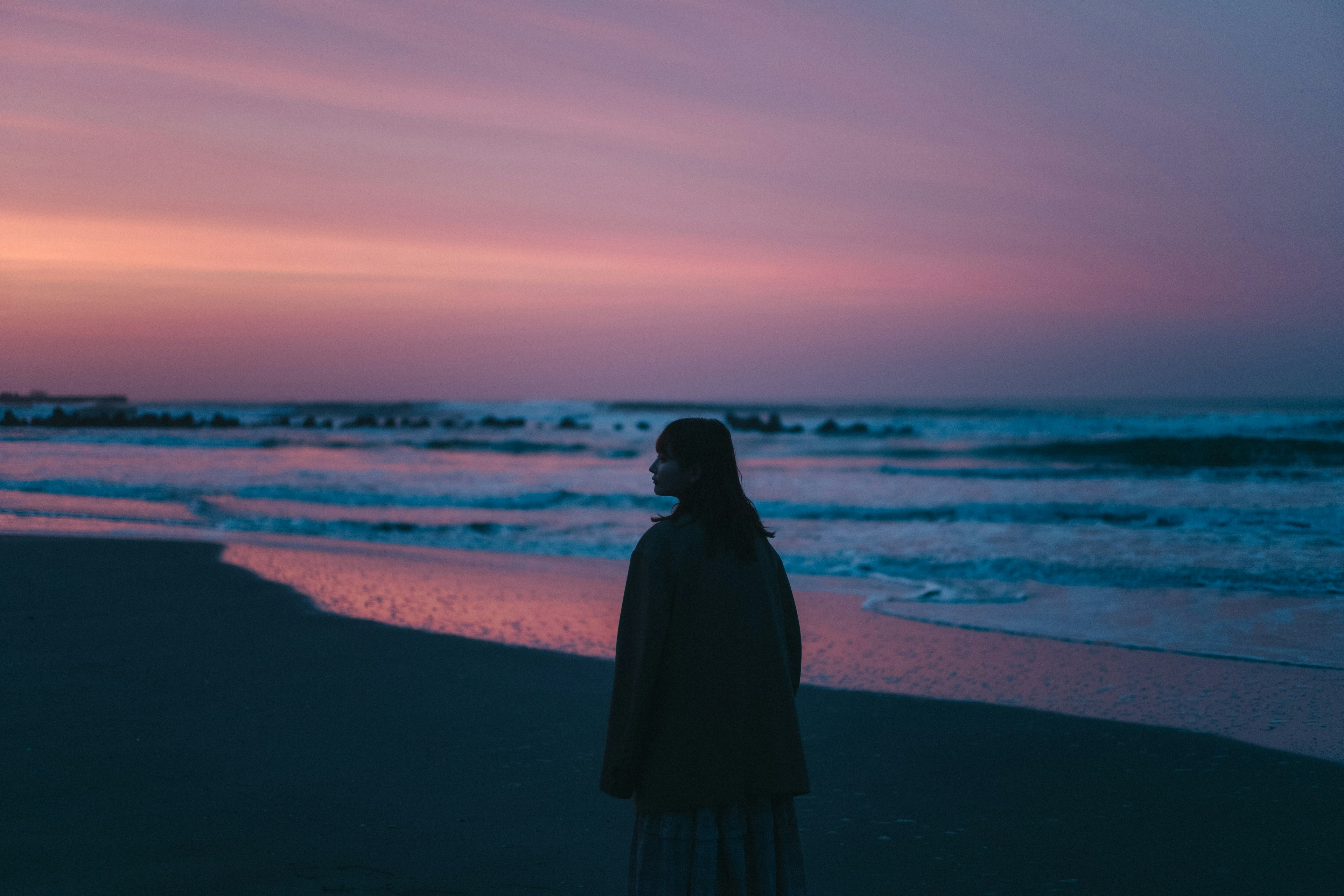 Siluet seorang wanita yang menatap matahari terbenam di pantai