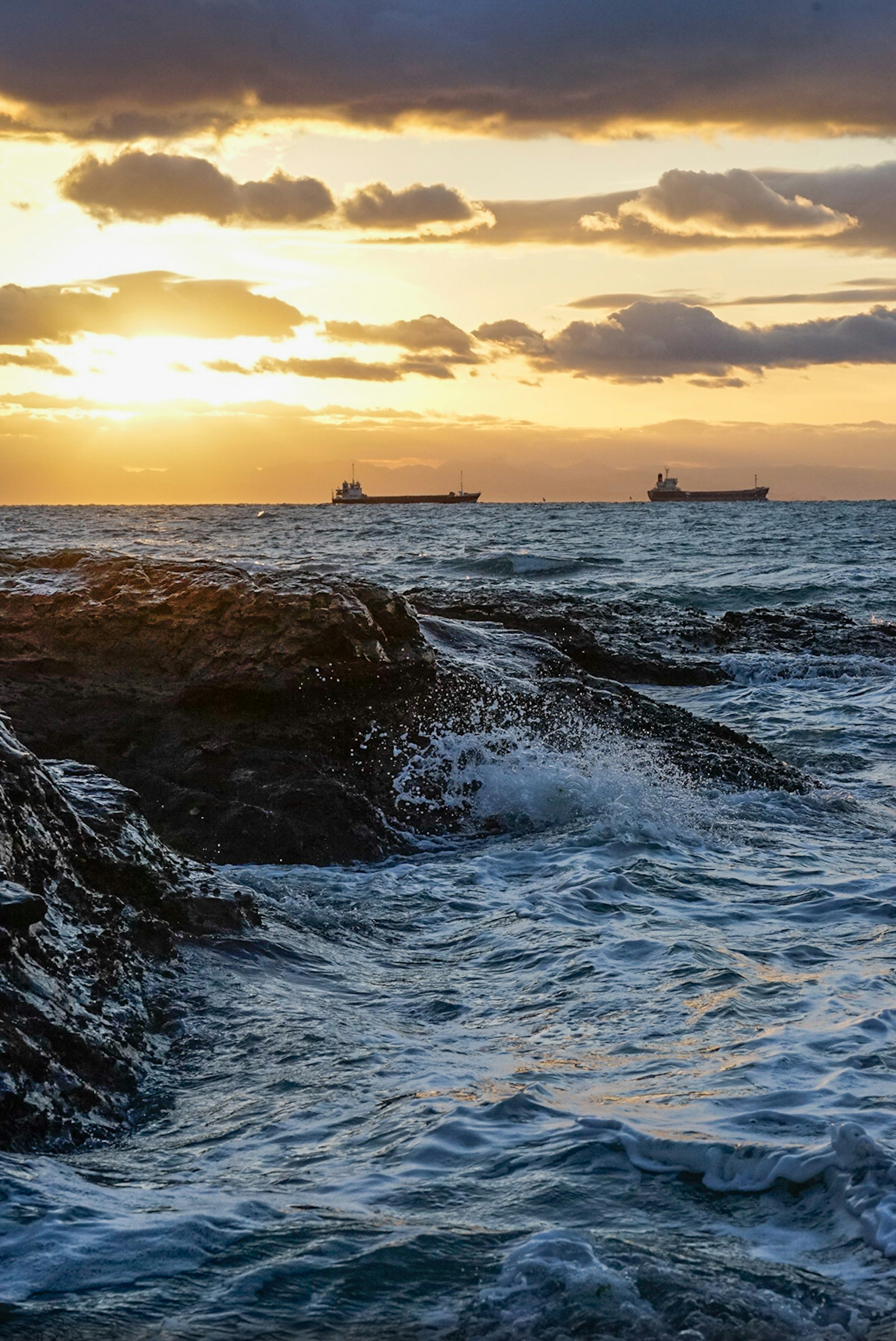 Felsenstrand bei Sonnenuntergang mit Schiffen in der Ferne