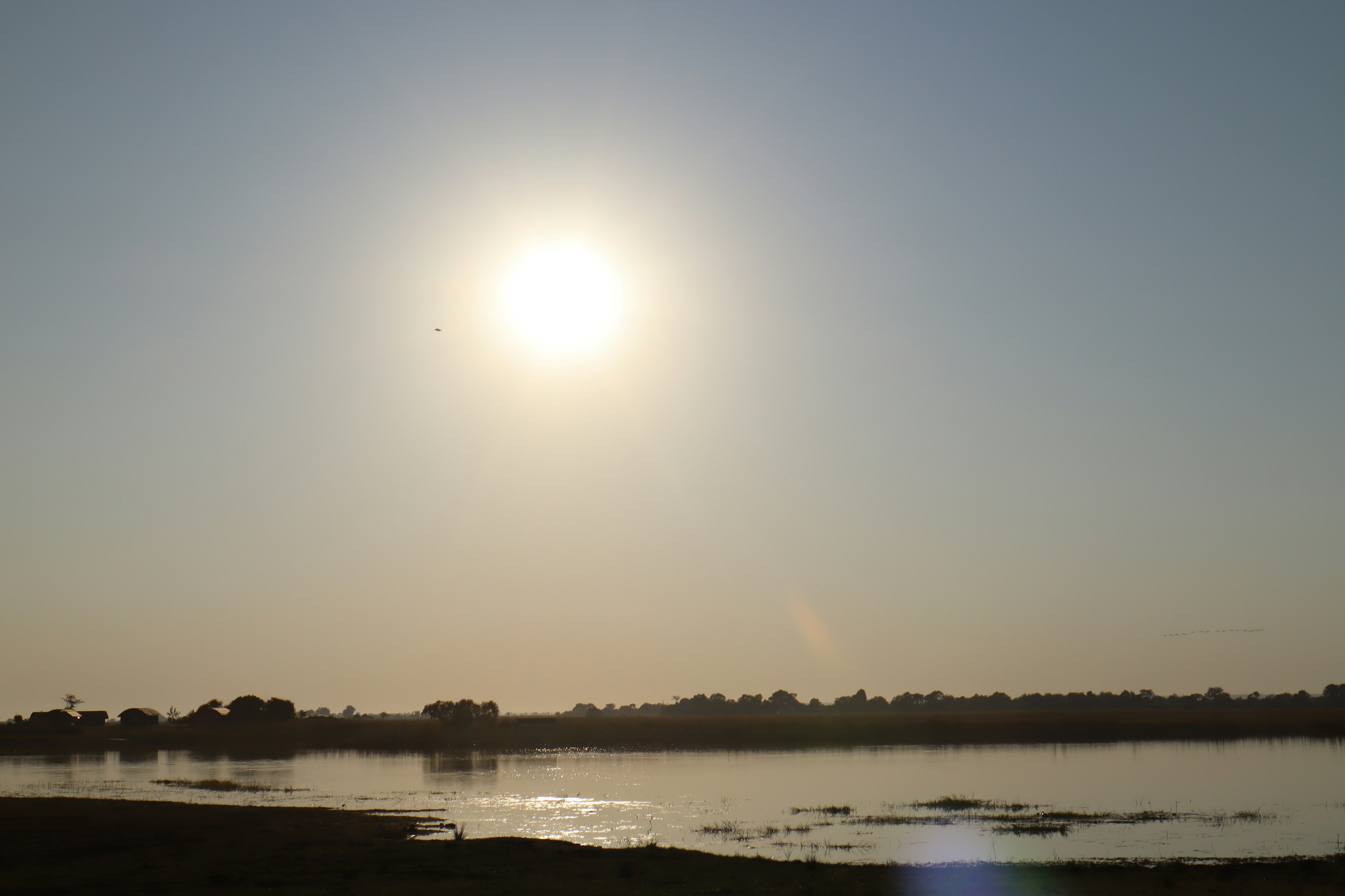 A serene landscape with the sun shining over calm waters and blue sky