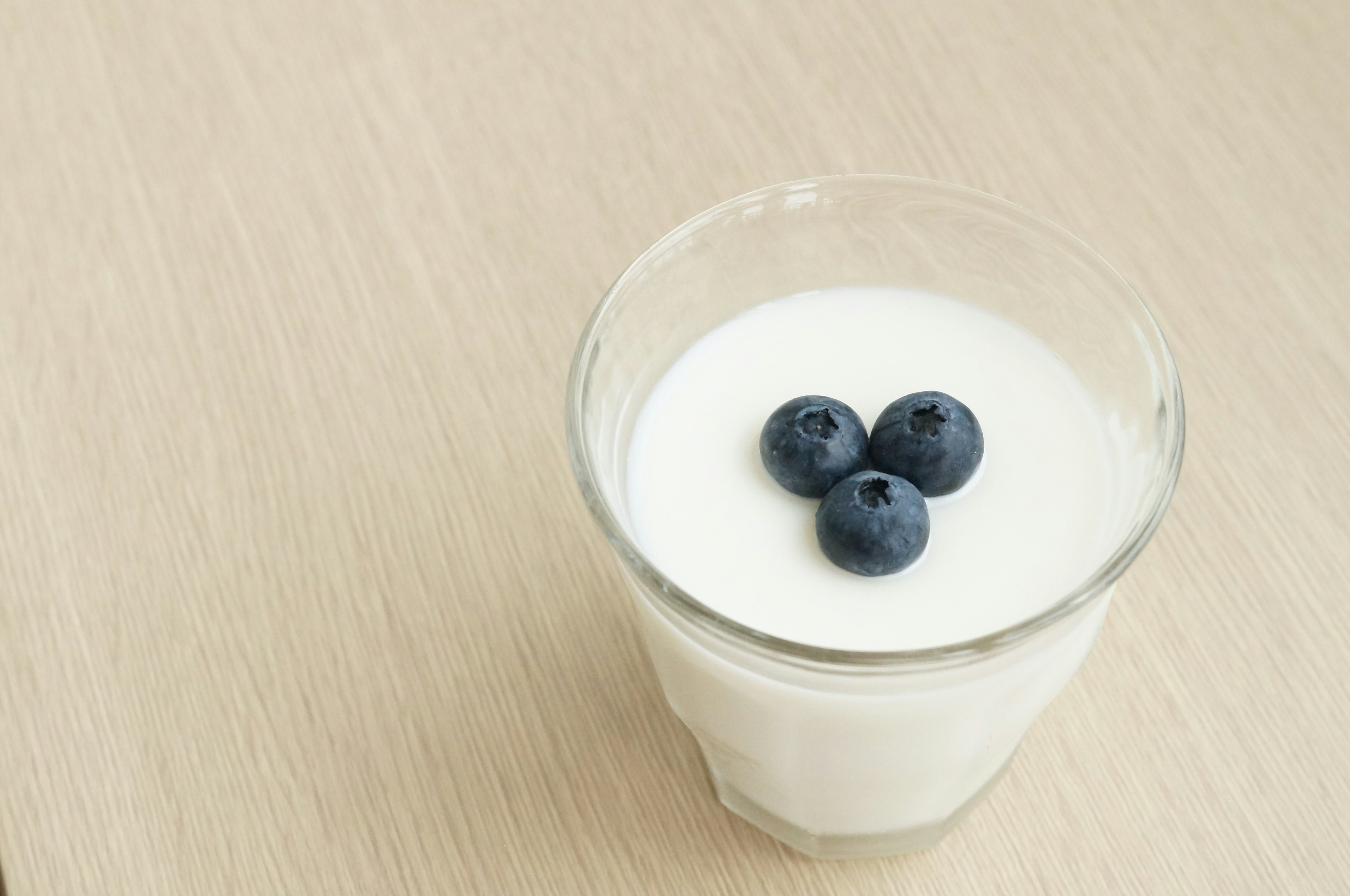 A clear glass of yogurt topped with three blueberries