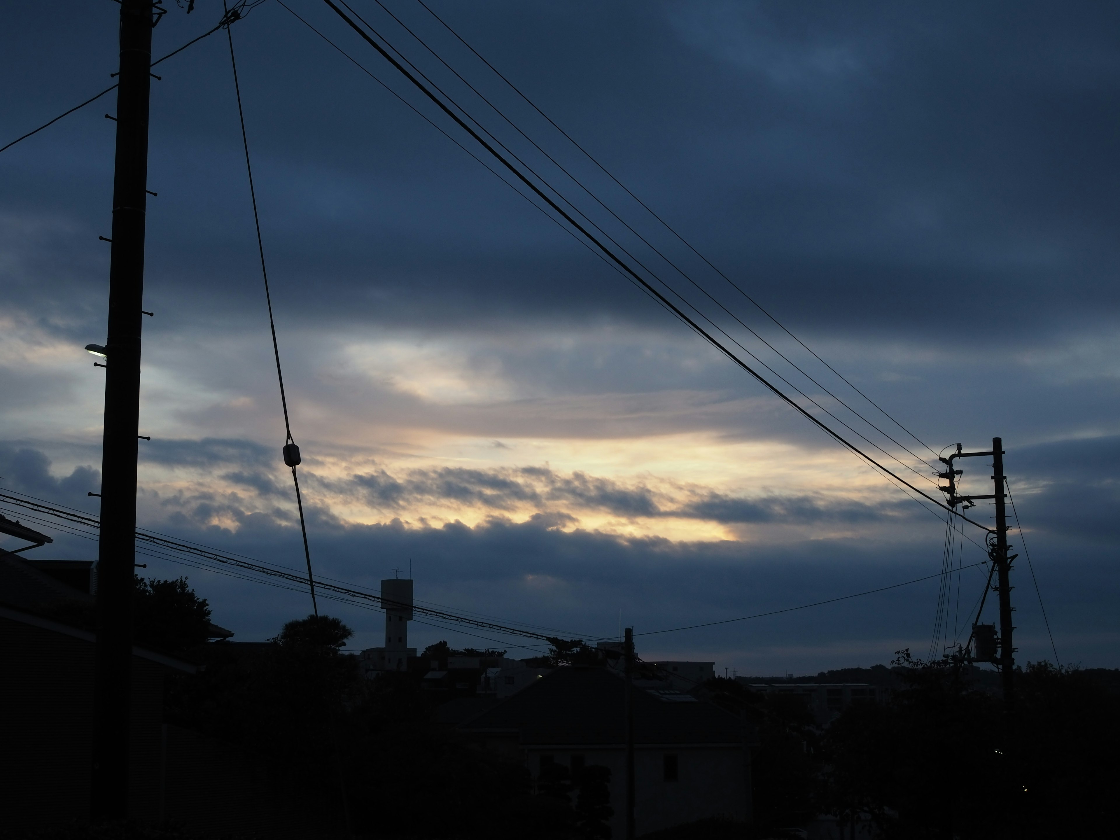 Un paysage avec une lumière crépusculaire sous un ciel nuageux avec des poteaux et des fils électriques