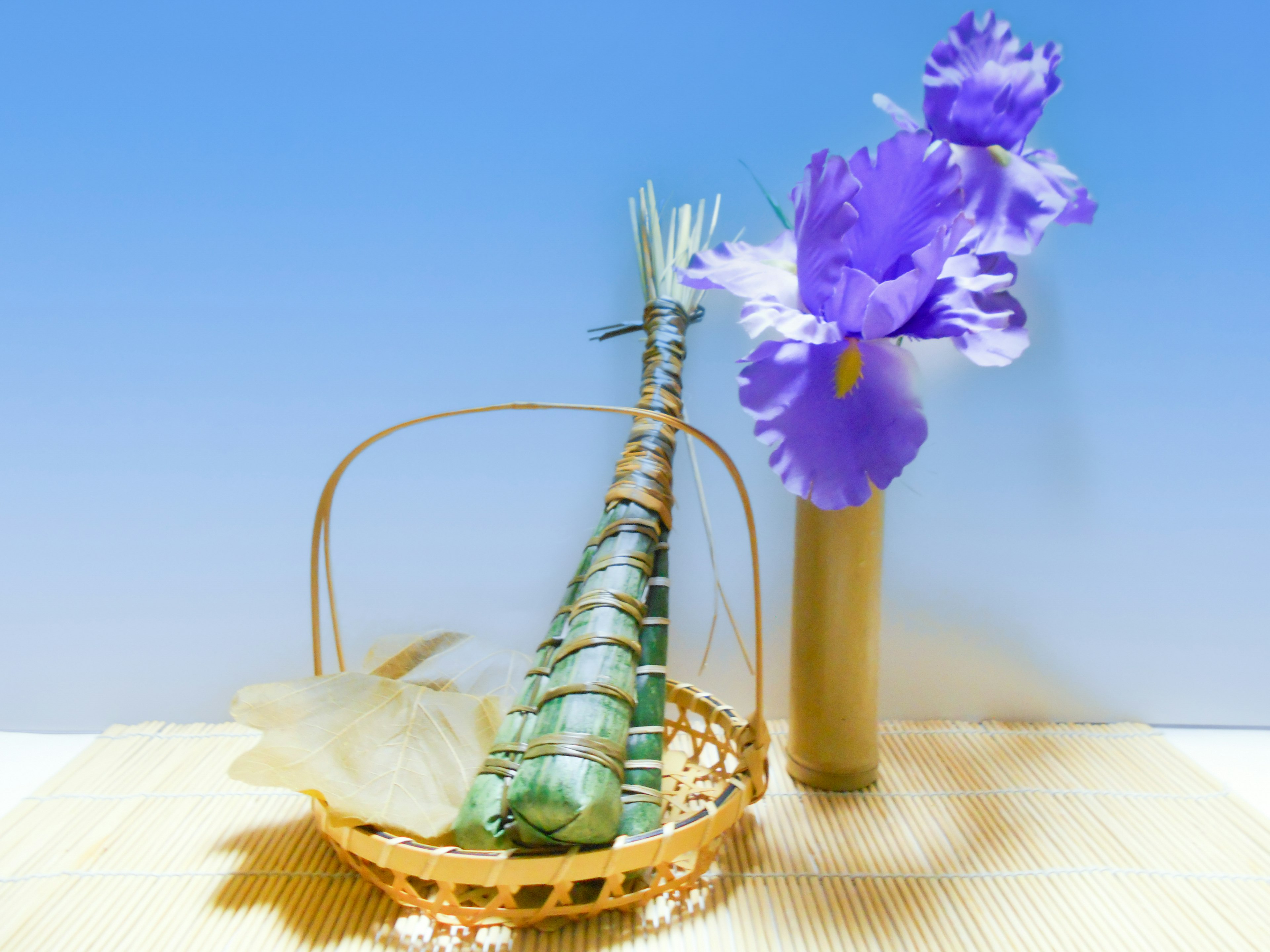 A basket with bamboo-like object and purple flowers against a blue sky background