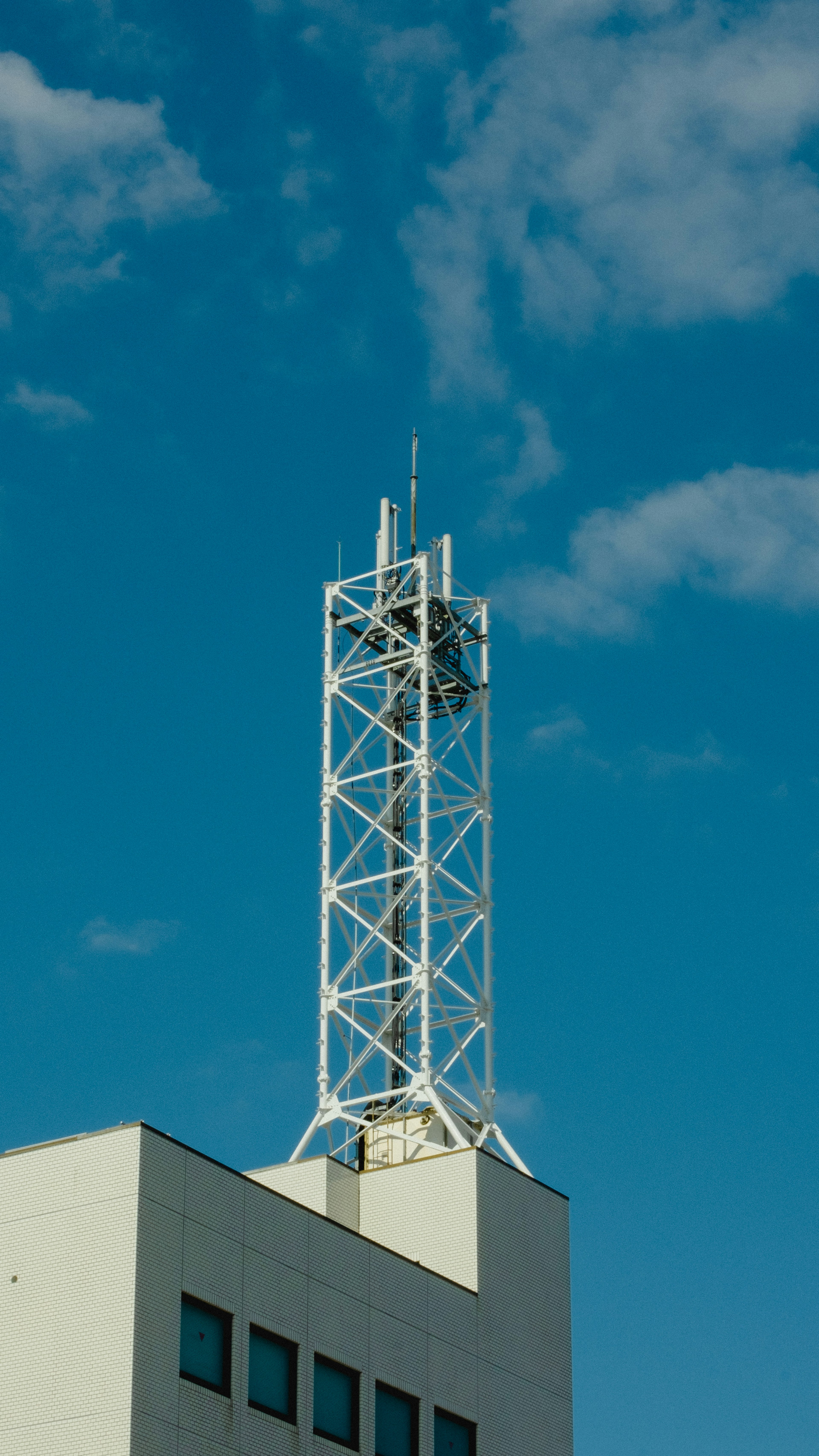 White communication tower against a blue sky with clouds