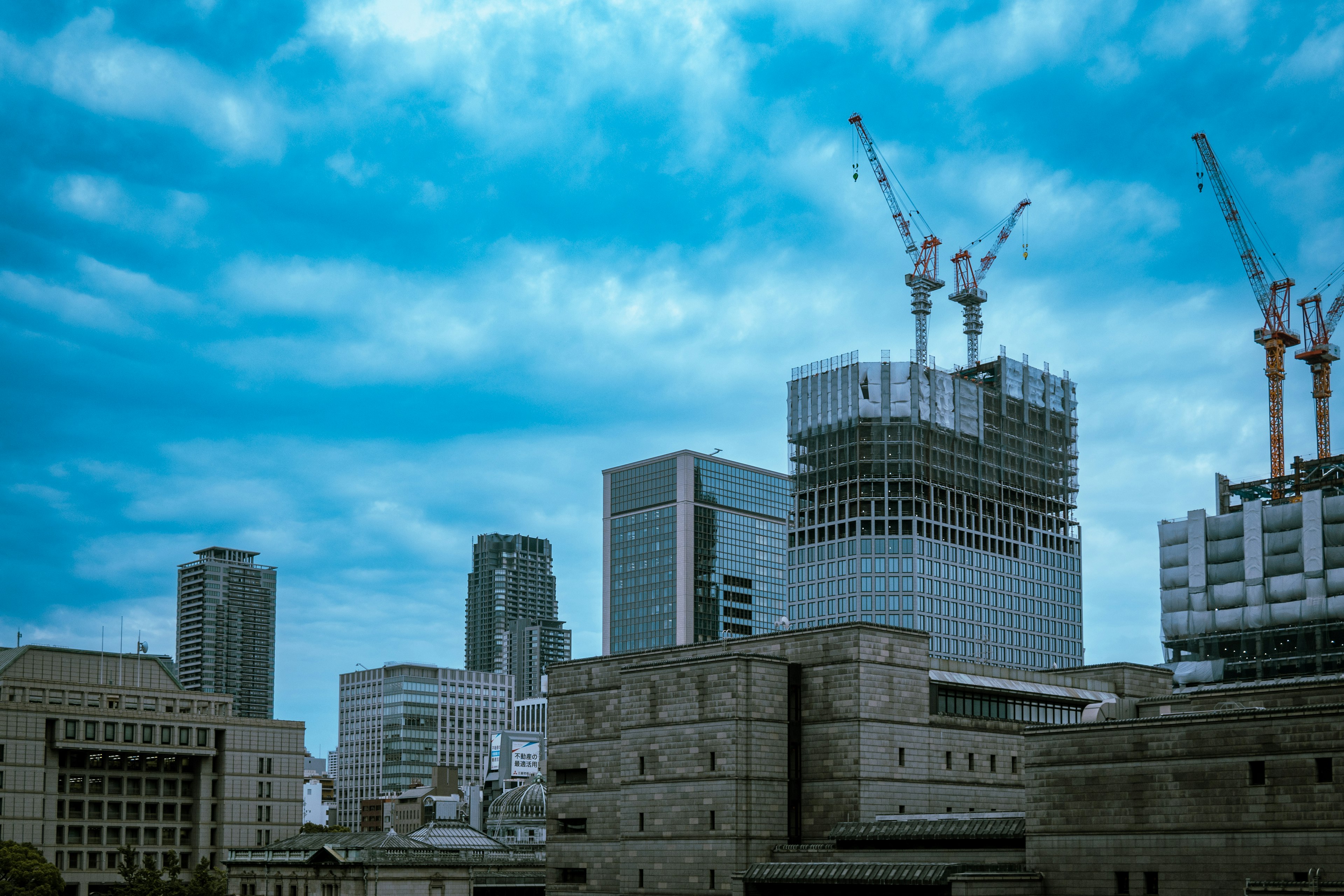 City skyline featuring construction cranes and modern buildings under a blue sky