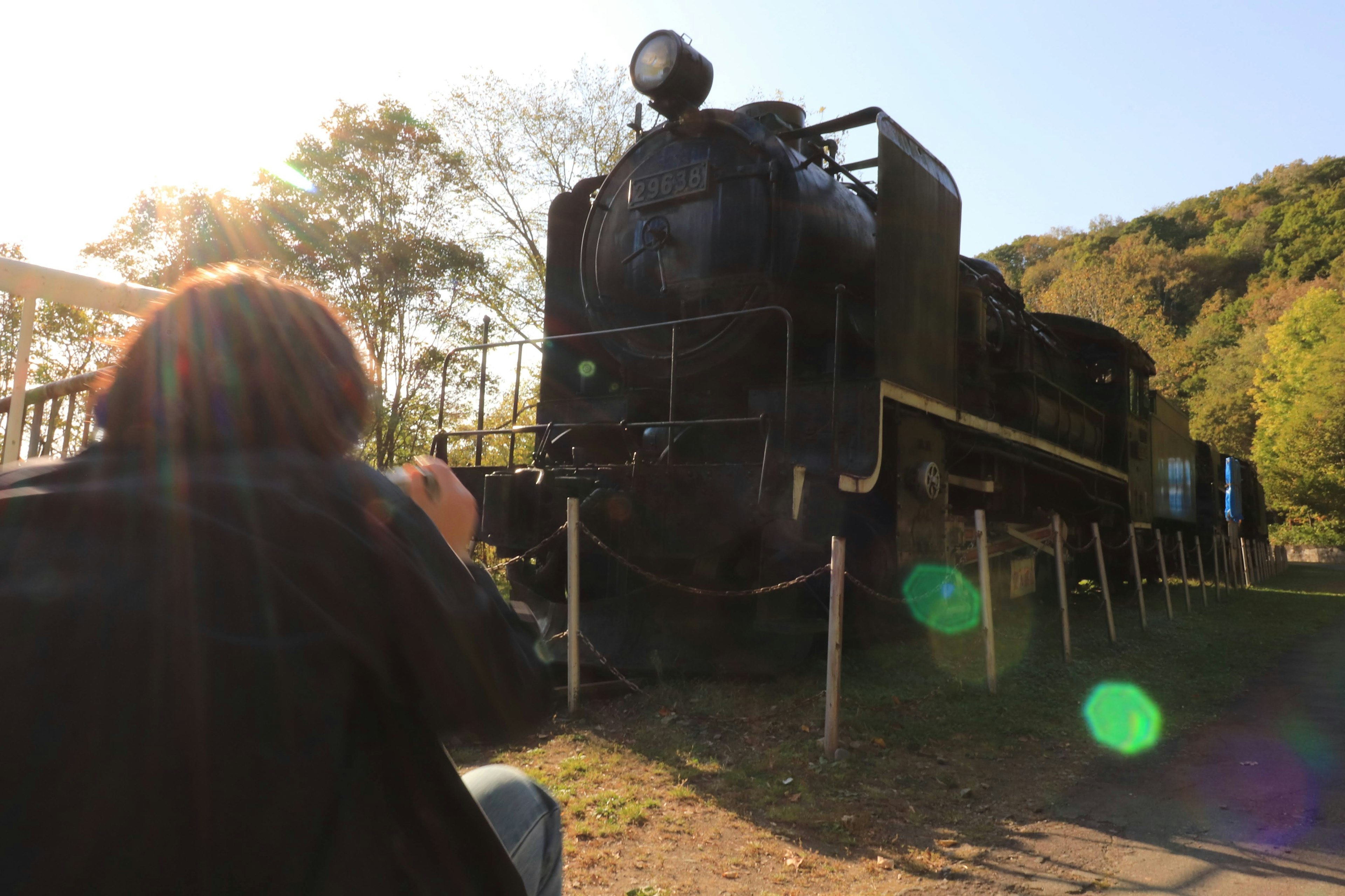 Silhouette d'une personne photographiant une locomotive à vapeur noire avec la lumière du soleil en arrière-plan