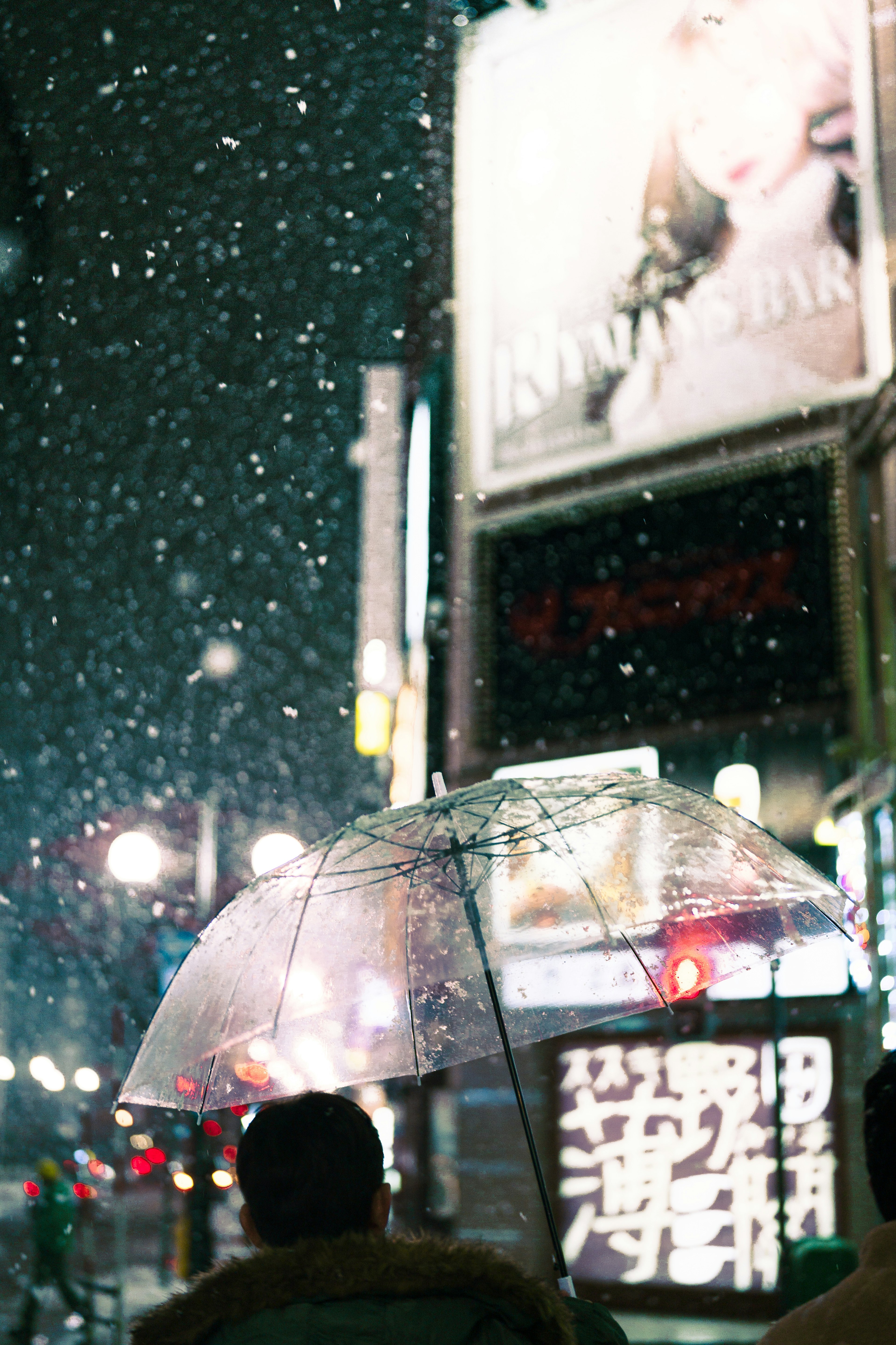 在下雪的夜晚街頭拿著透明雨傘的人