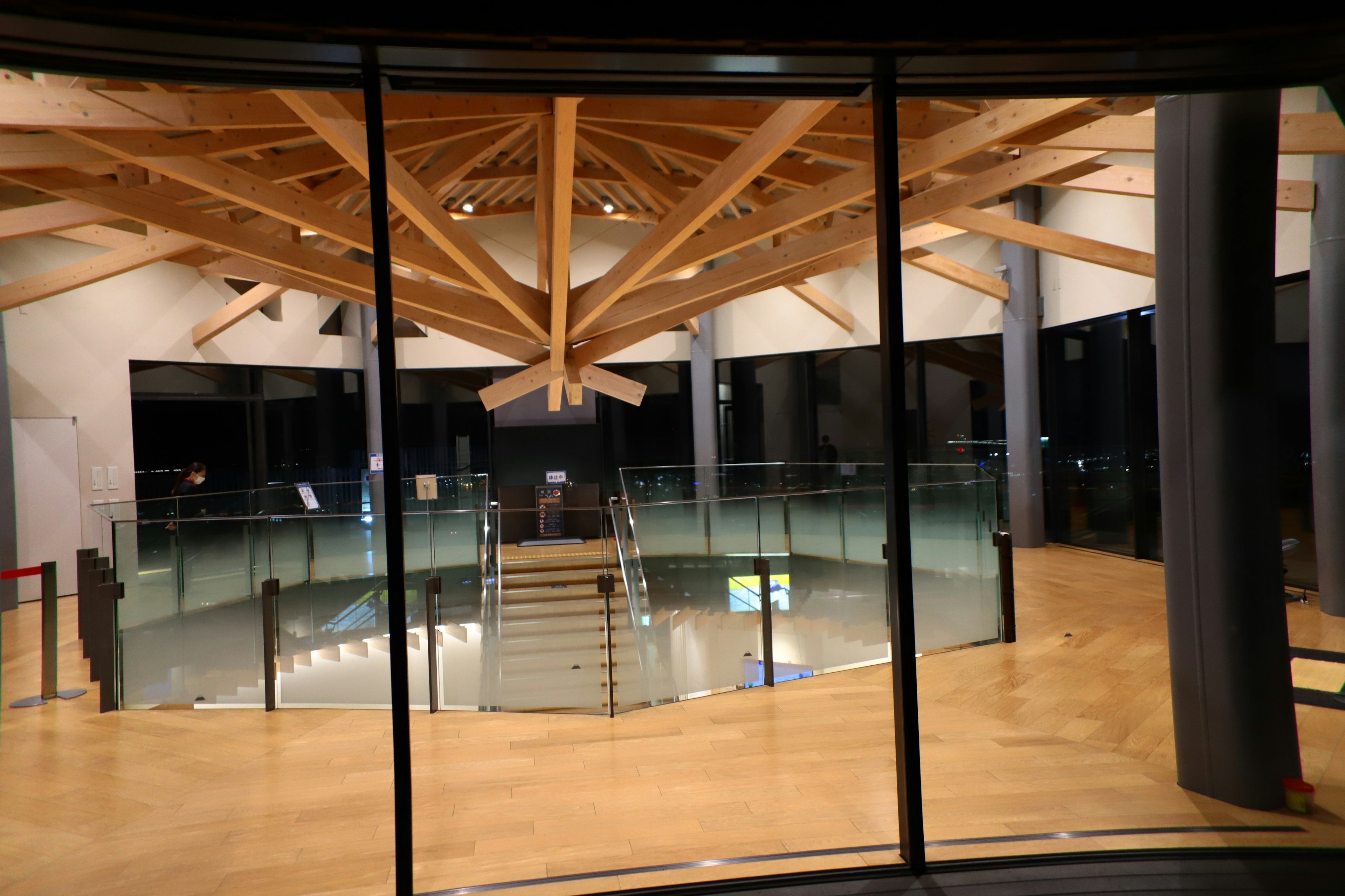 Interior de un edificio moderno con vigas de madera y paredes de vidrio, con una escalera central