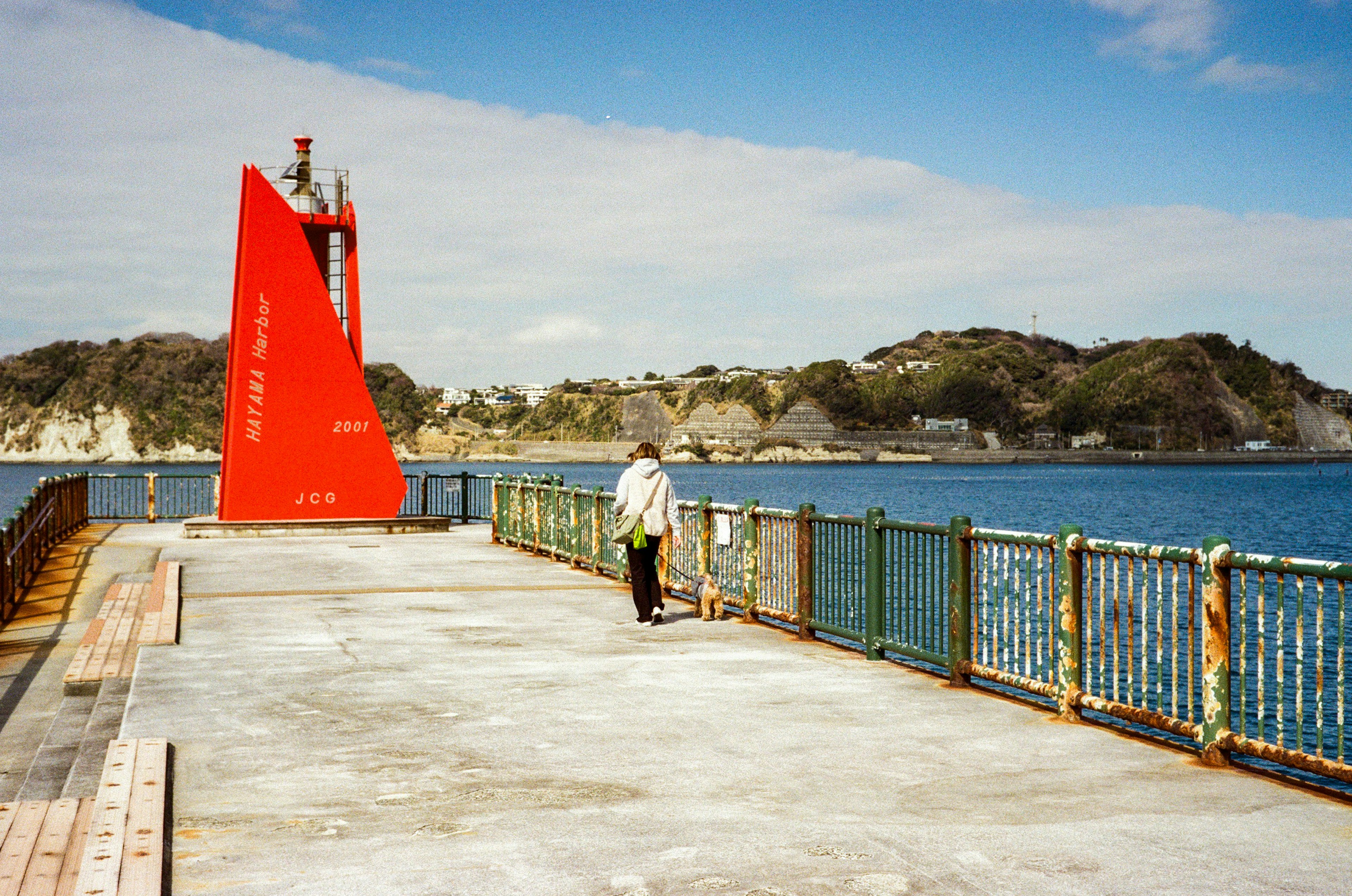 Una persona de pie en un muelle con un faro rojo al fondo