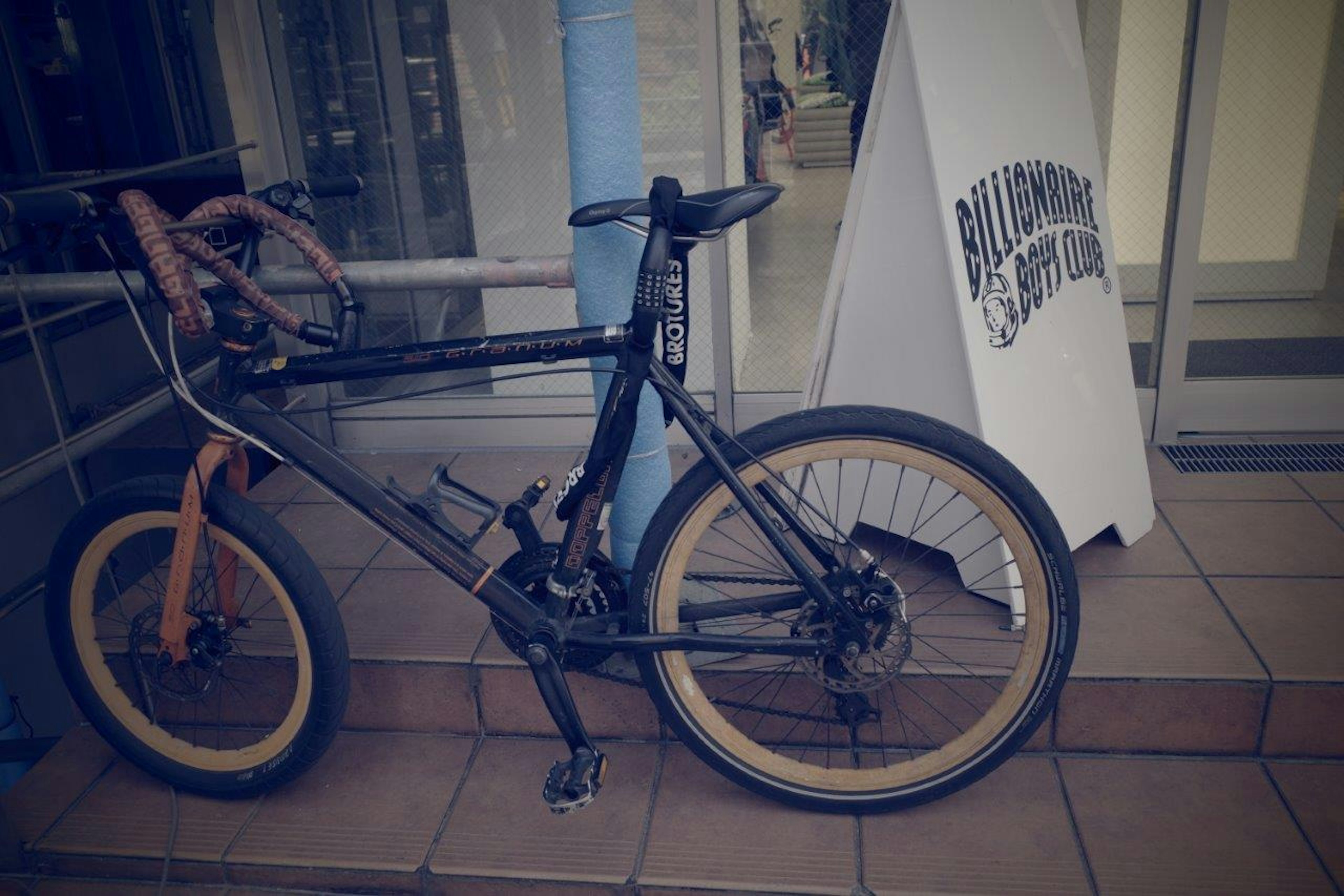 A black bicycle with an orange handlebar leaning against a wall