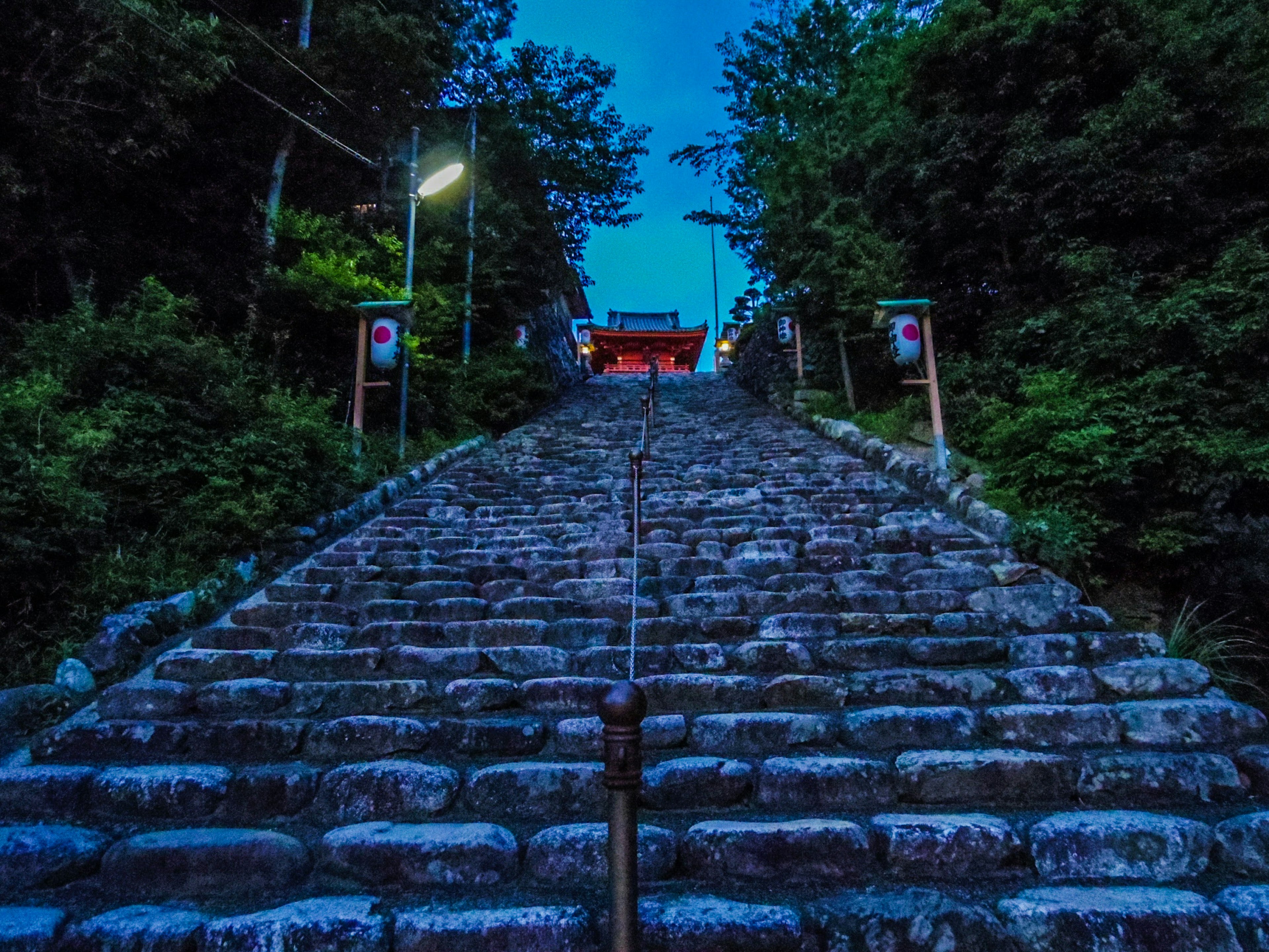 Stone steps leading up to a shrine illuminated by lights under a blue night sky