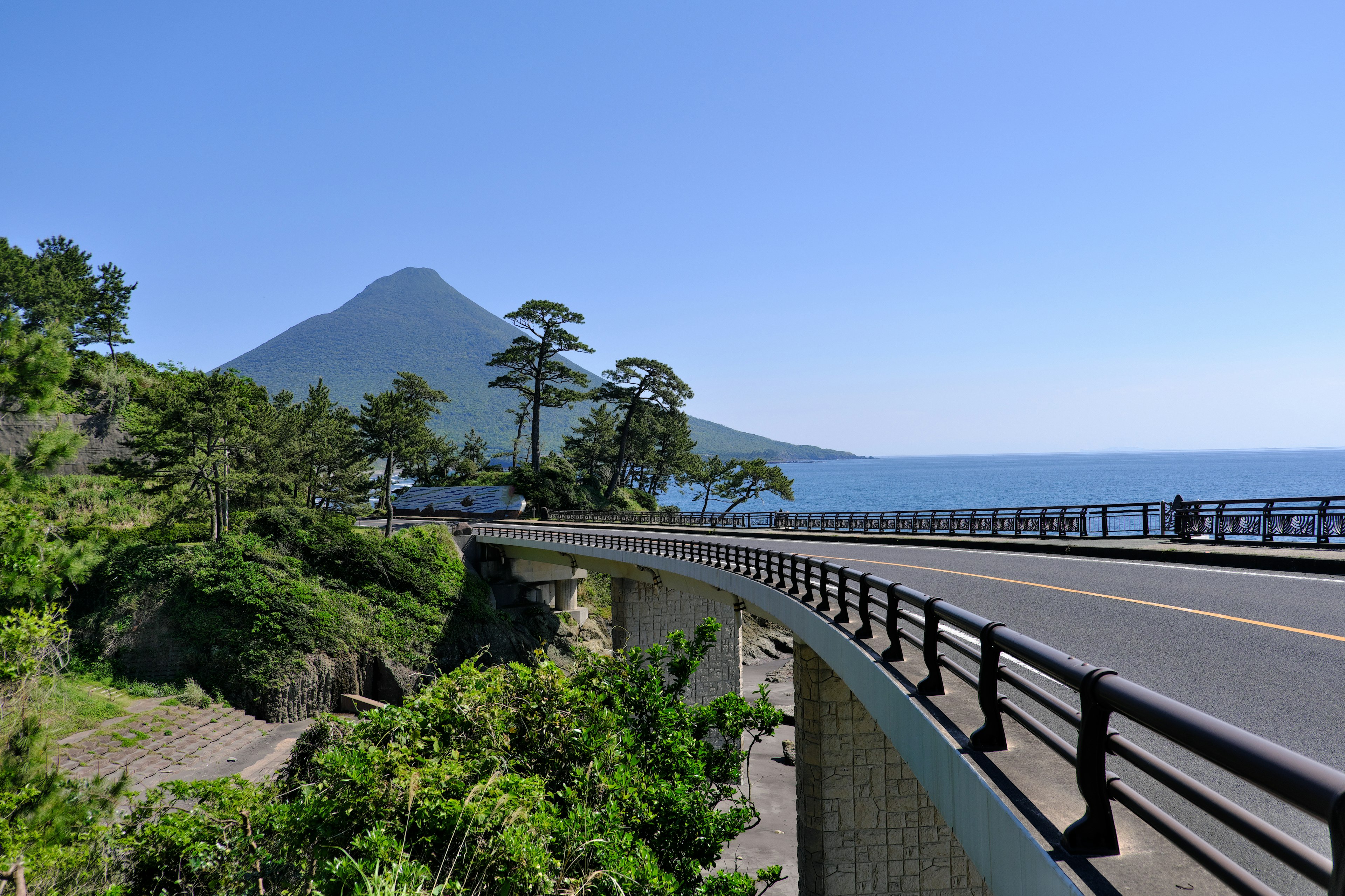 Route sinueuse au bord de la mer avec une montagne en arrière-plan sous un ciel bleu clair