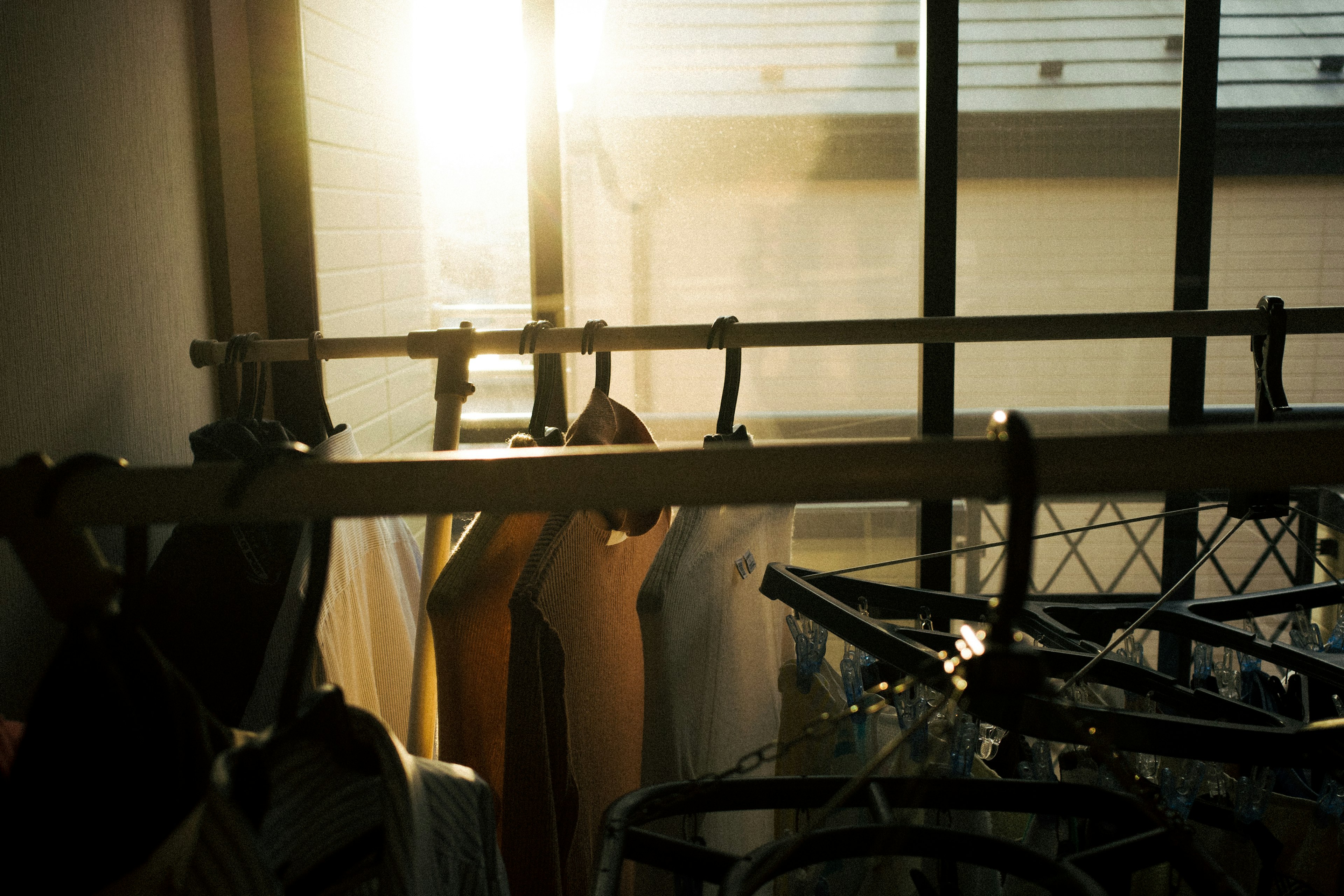 Clothes hanging on a rack with bicycles visible in the warm light from the window