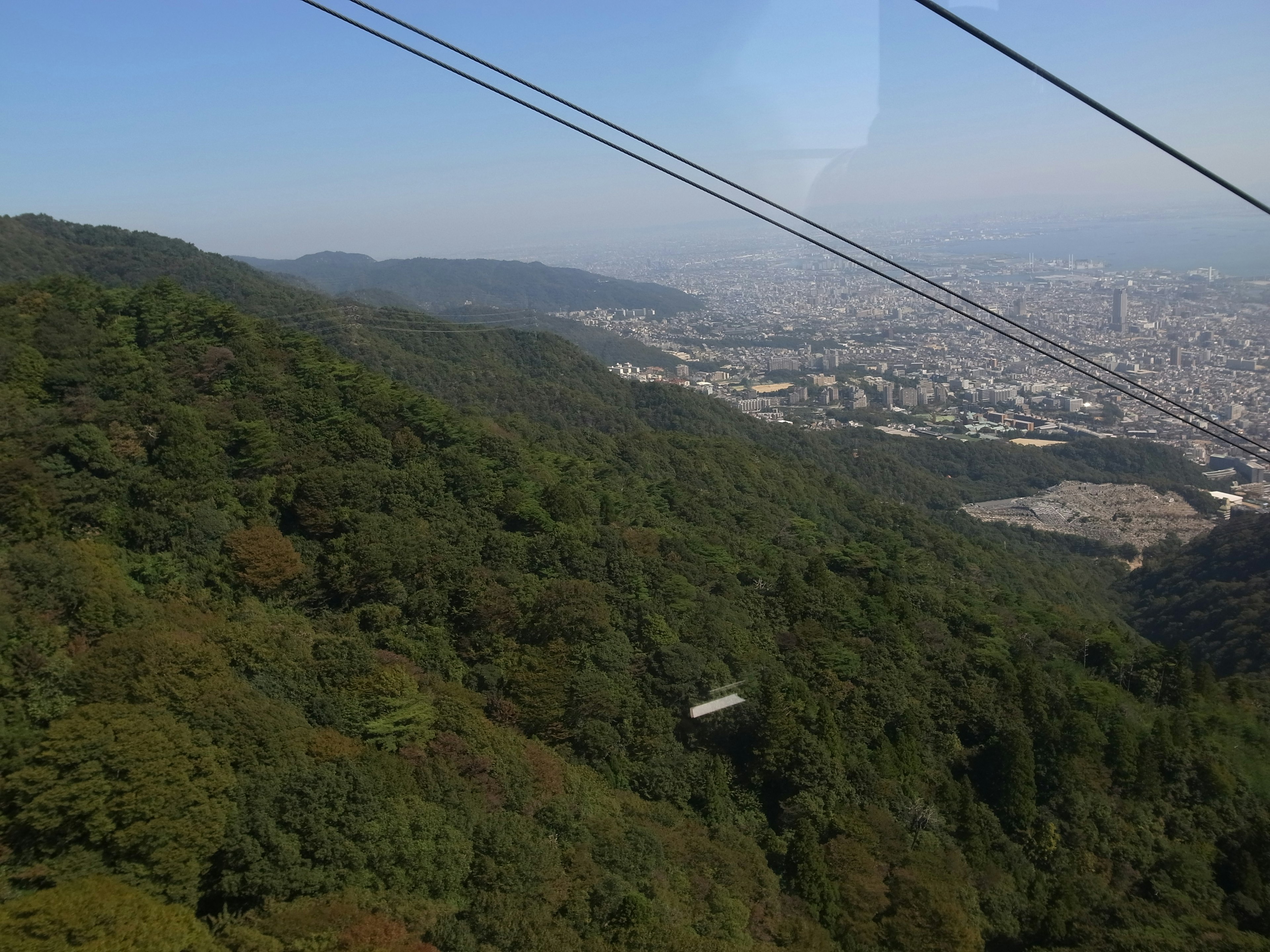 Scenic view from a cable car overlooking lush green mountains and a city skyline