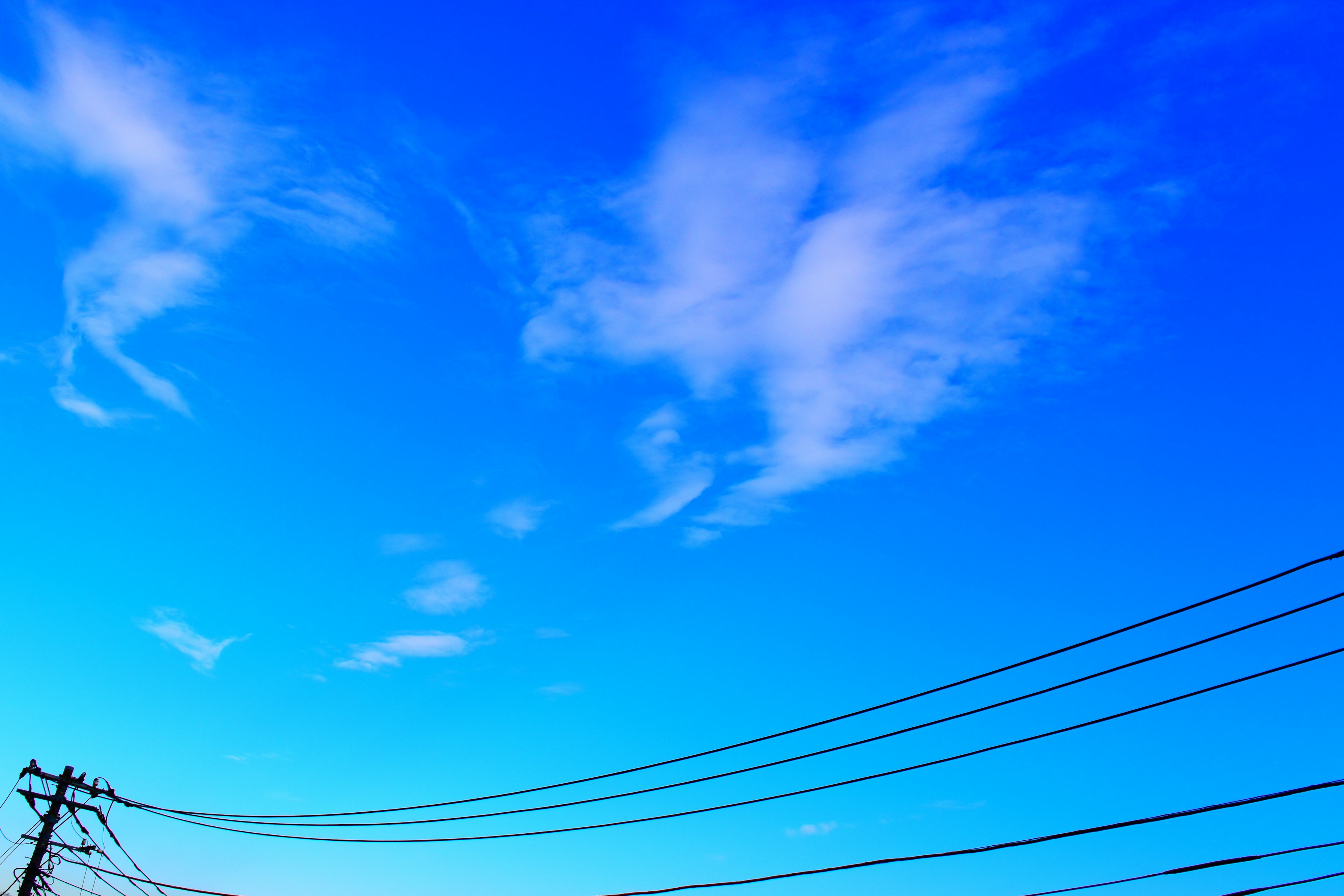 Vibrant blue sky with wispy white clouds power lines stretching across the bottom